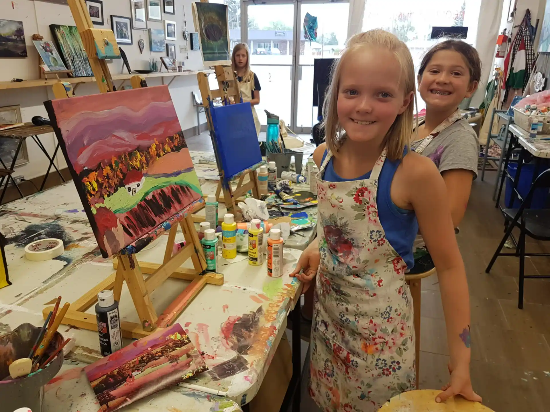 a couple of girls posing for a picture next to a table with art