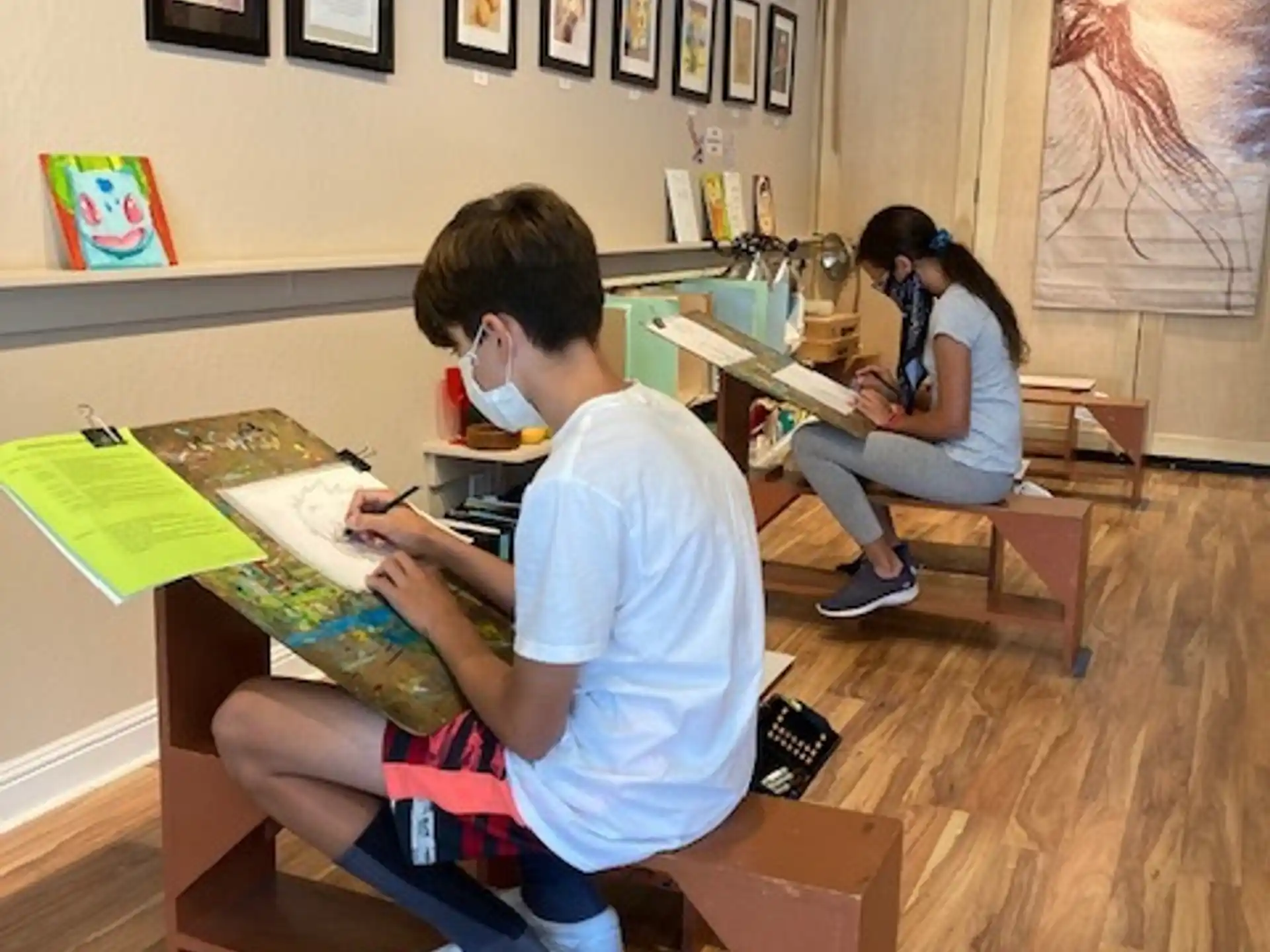 a boy and girl sitting at desks in a room with pictures on the wall