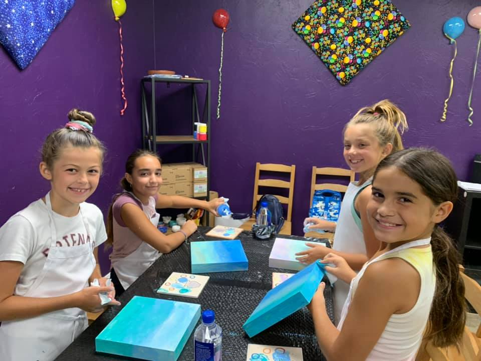 a group of girls sitting at a table with a blue box and balloons