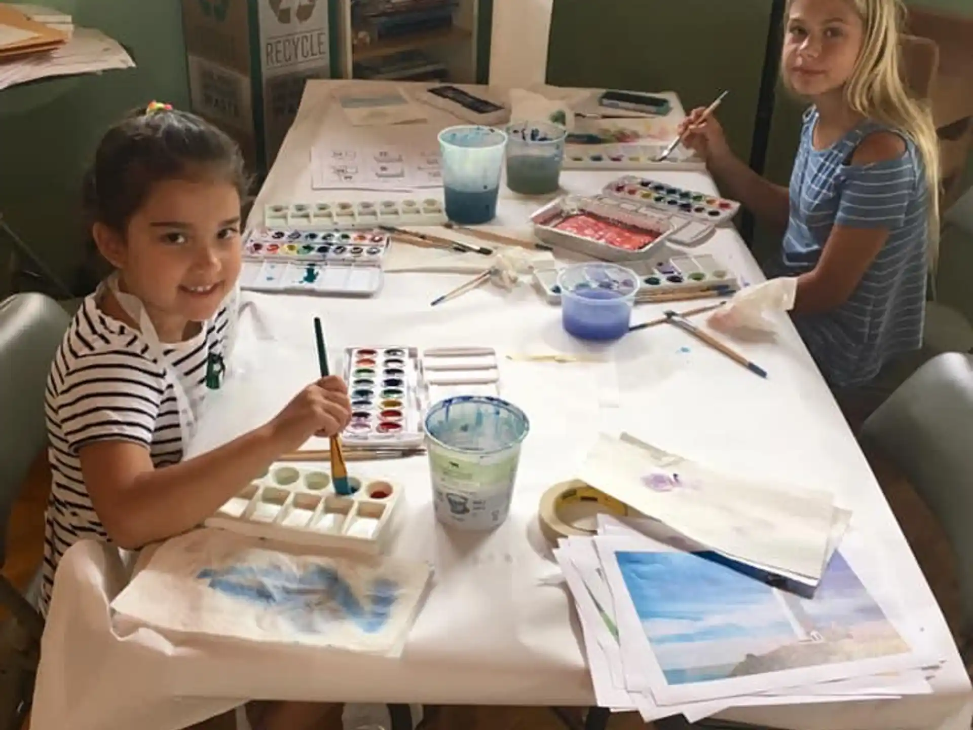 a couple of girls sitting at a table with a white board and a book and a pen