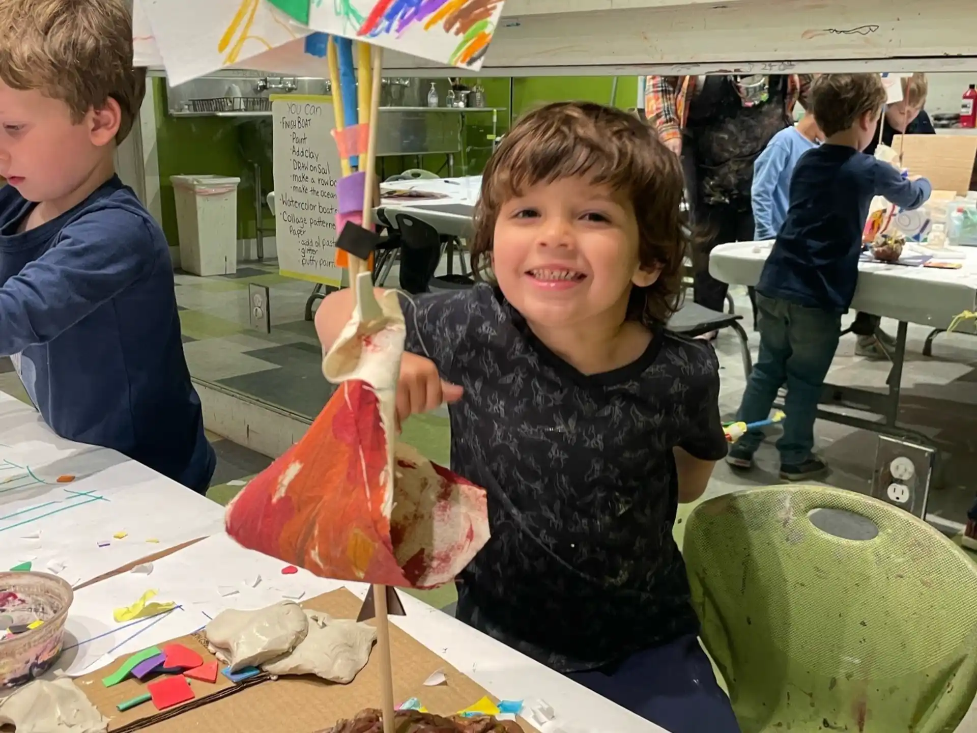 a boy sitting at a table with a kite and other people