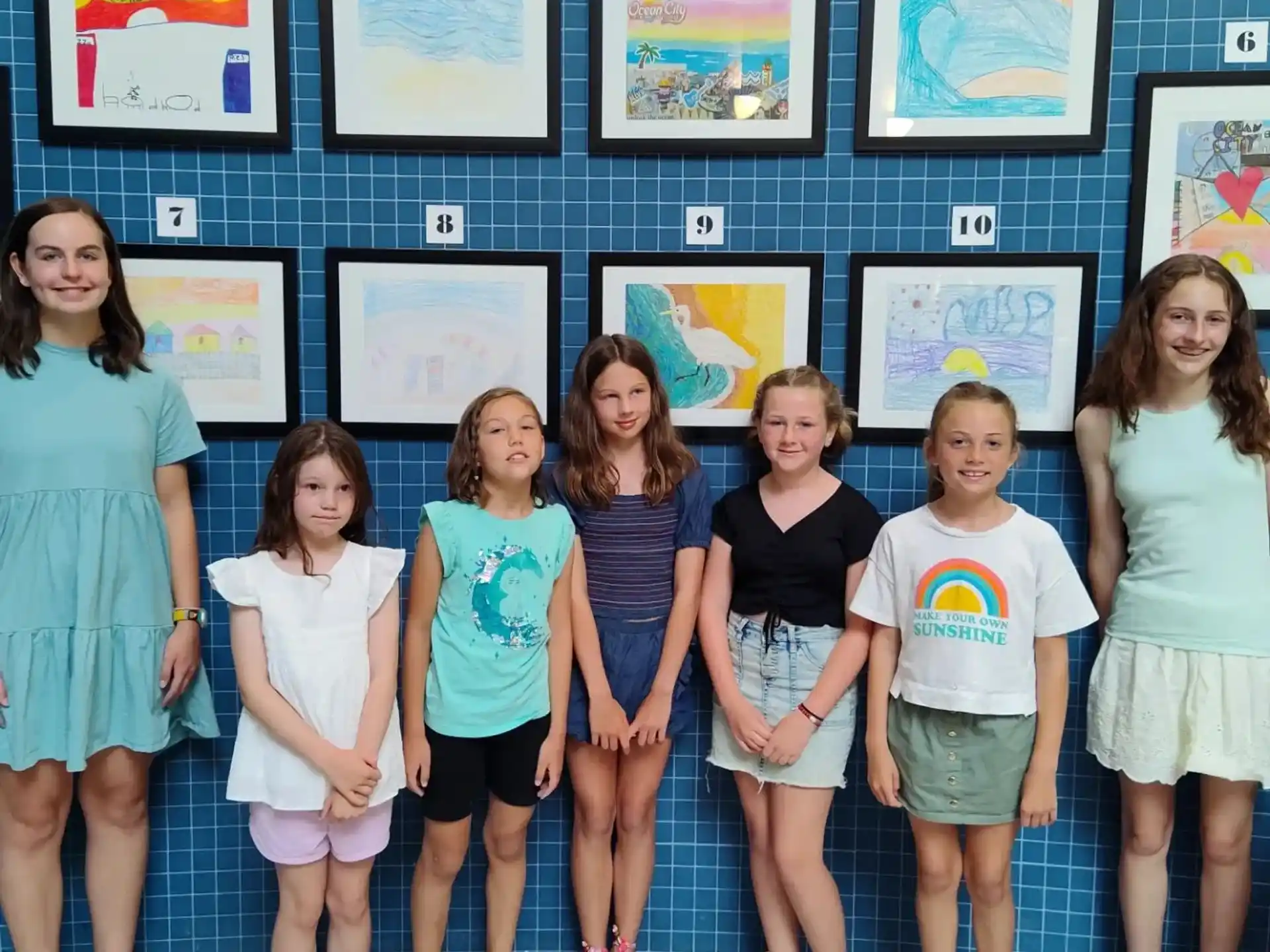 a group of girls posing for a photo in front of framed pictures