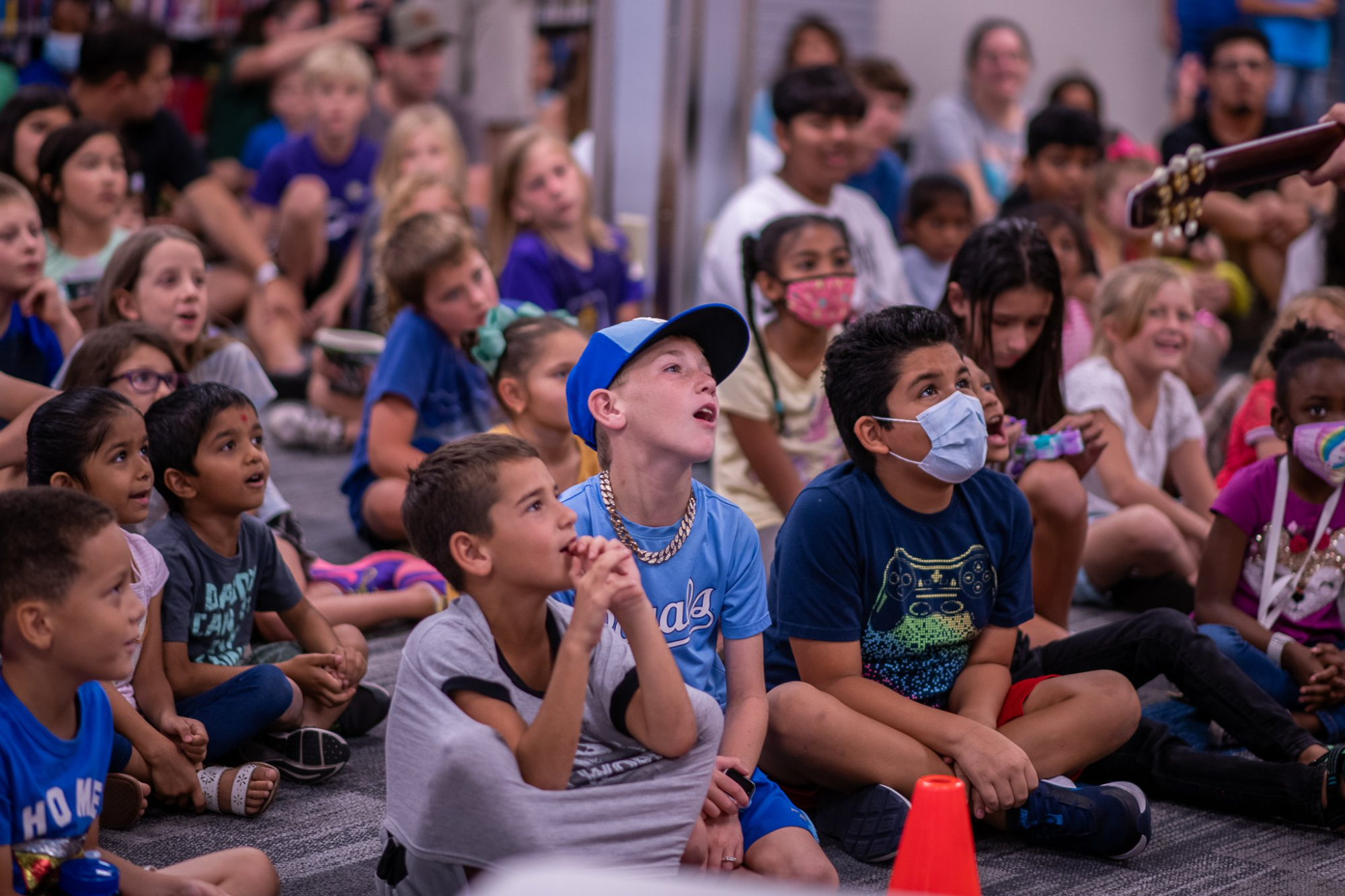a group of children sitting in a circle with a person wearing a mask