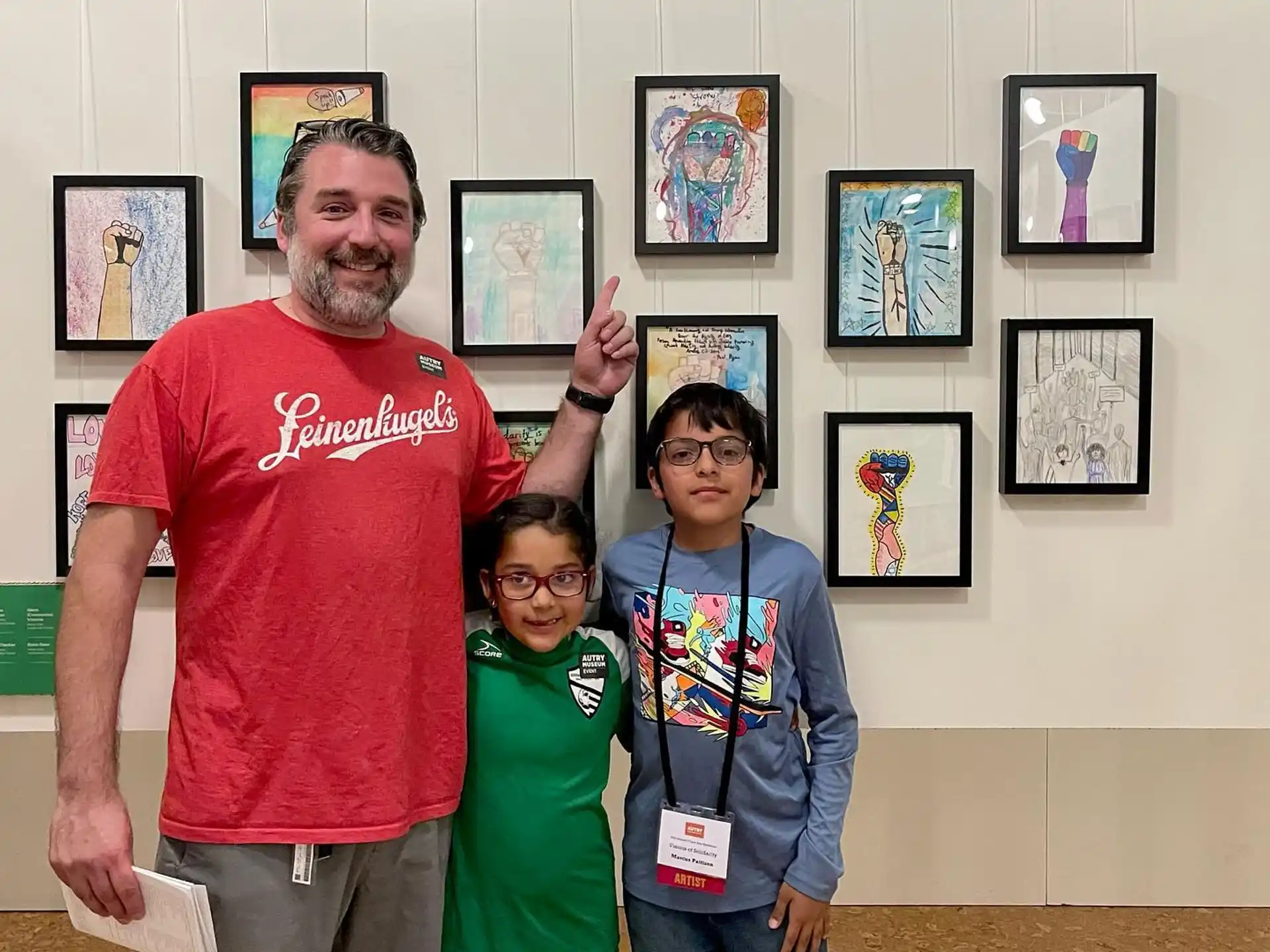 a group of people posing for a photo in front of a wall of framed pictures