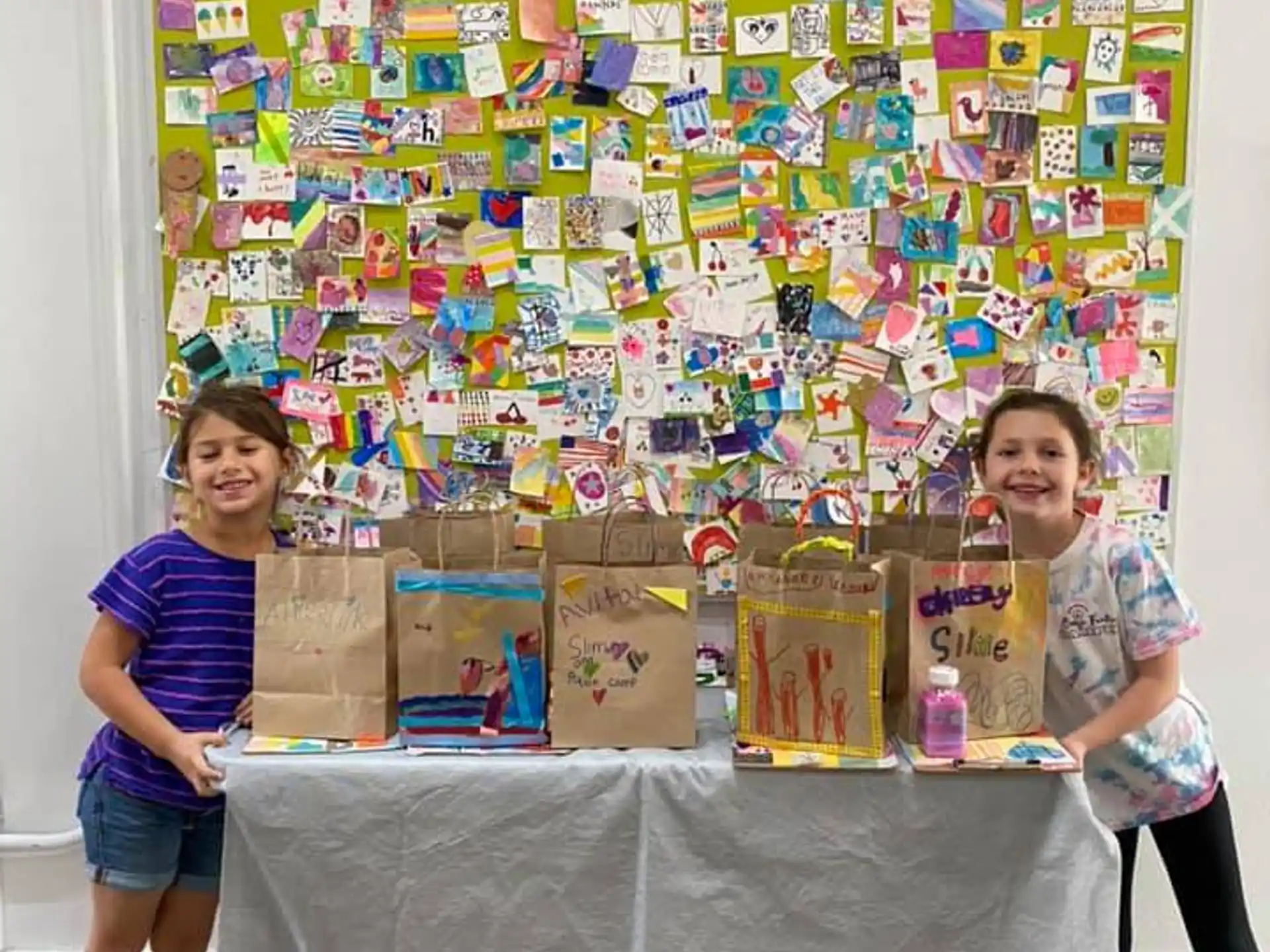 a couple of girls standing next to a table with a wall of art