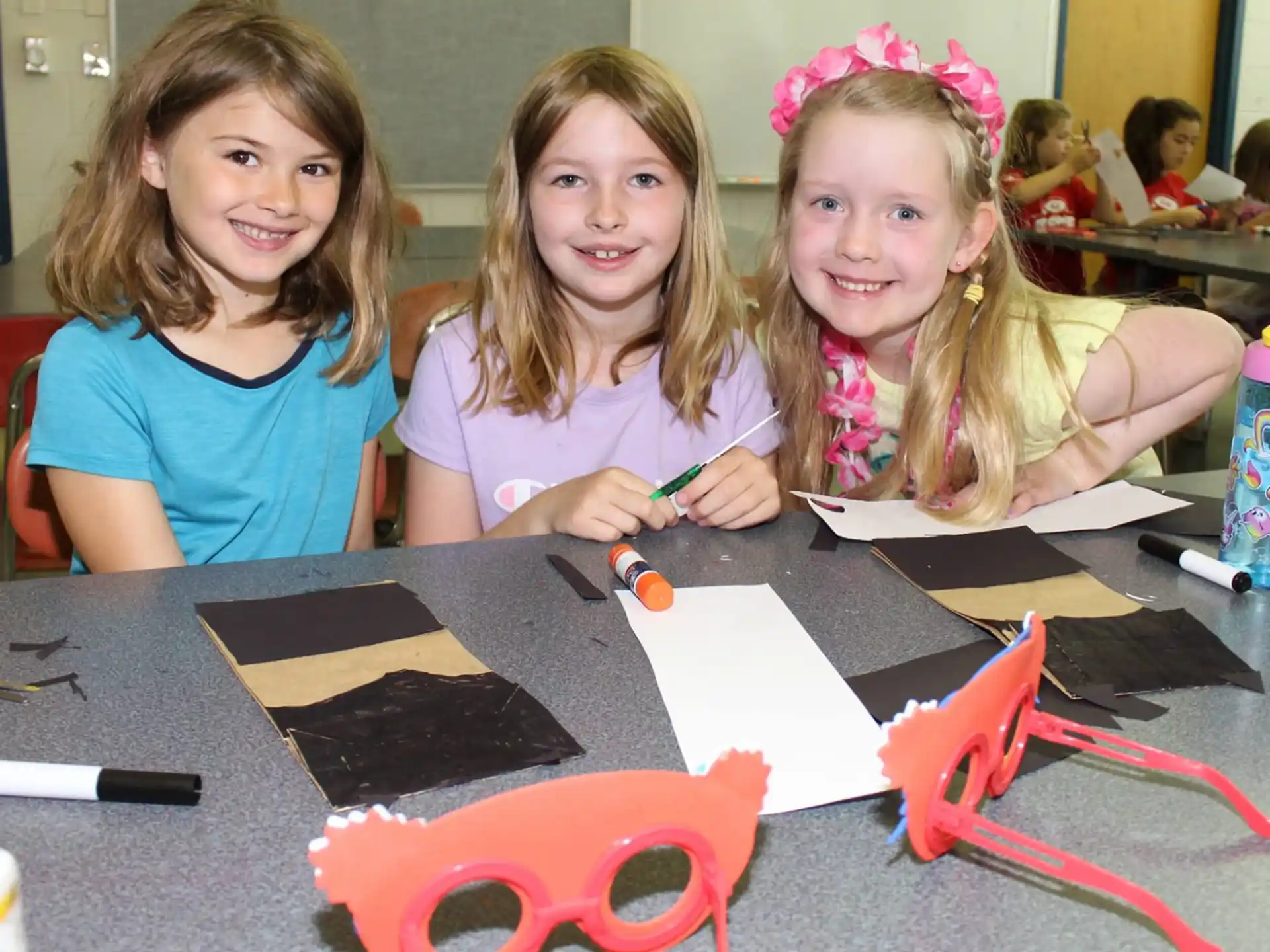 a group of girls sitting at a table with a book and pencils