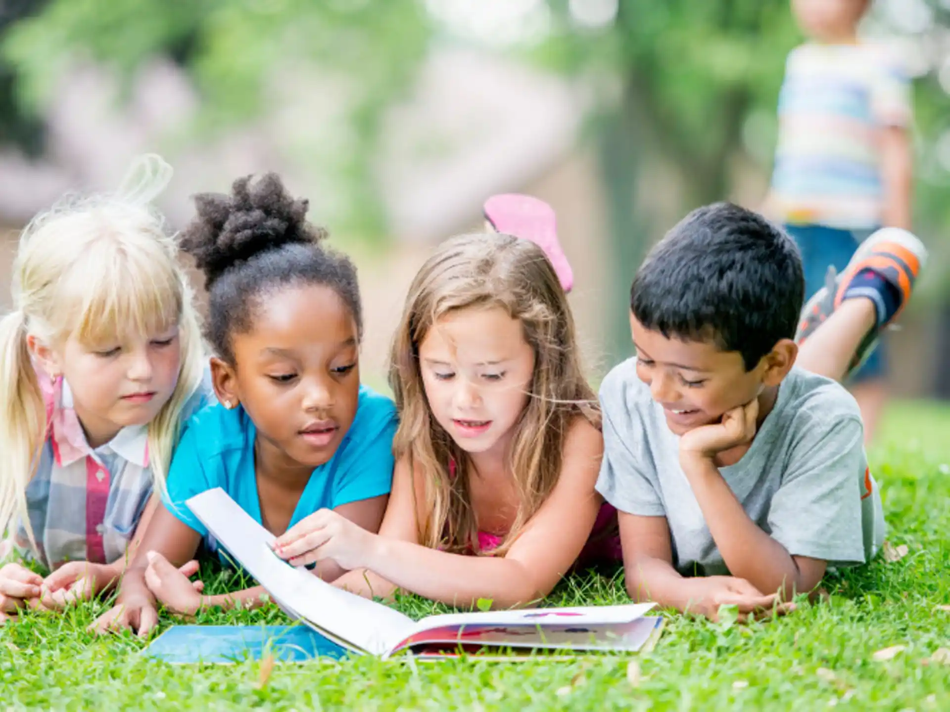 a group of children sitting on the grass looking at a book