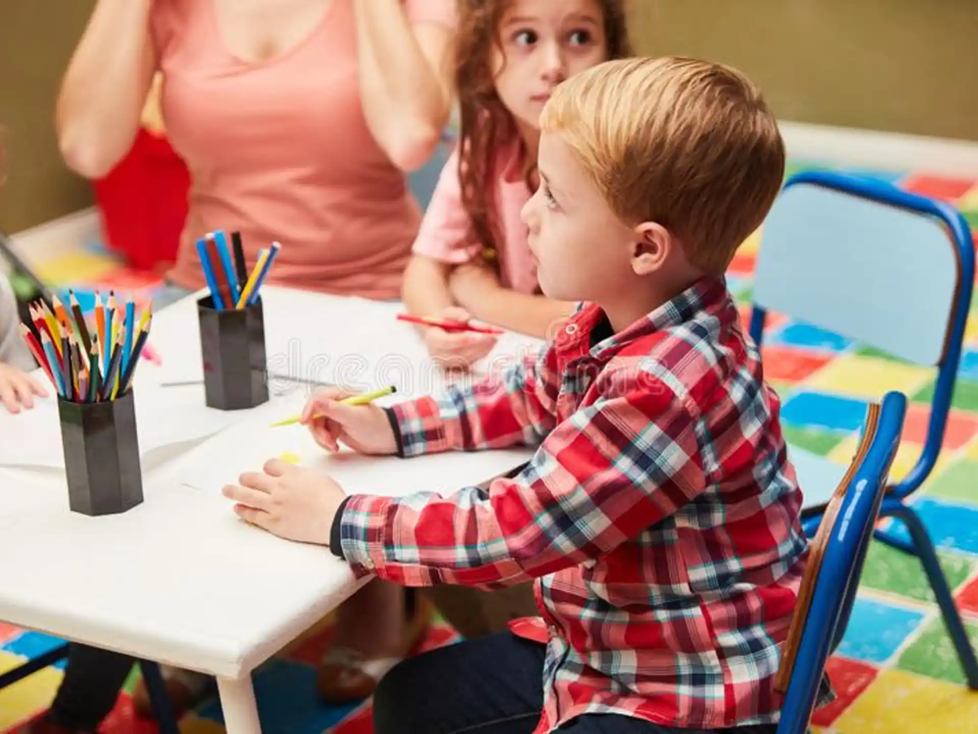 a group of children sitting at a table with pencils and pens