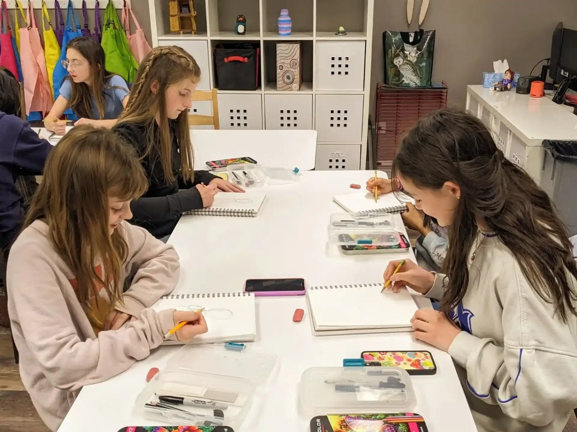 a group of women sitting at a table with books and drawings on it