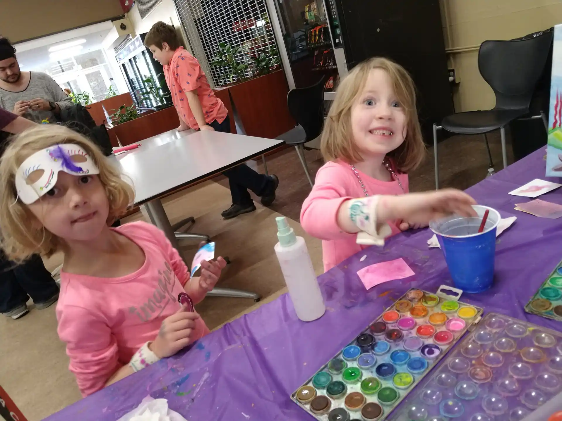 a couple of girls sitting at a table with colorful paper and a bottle