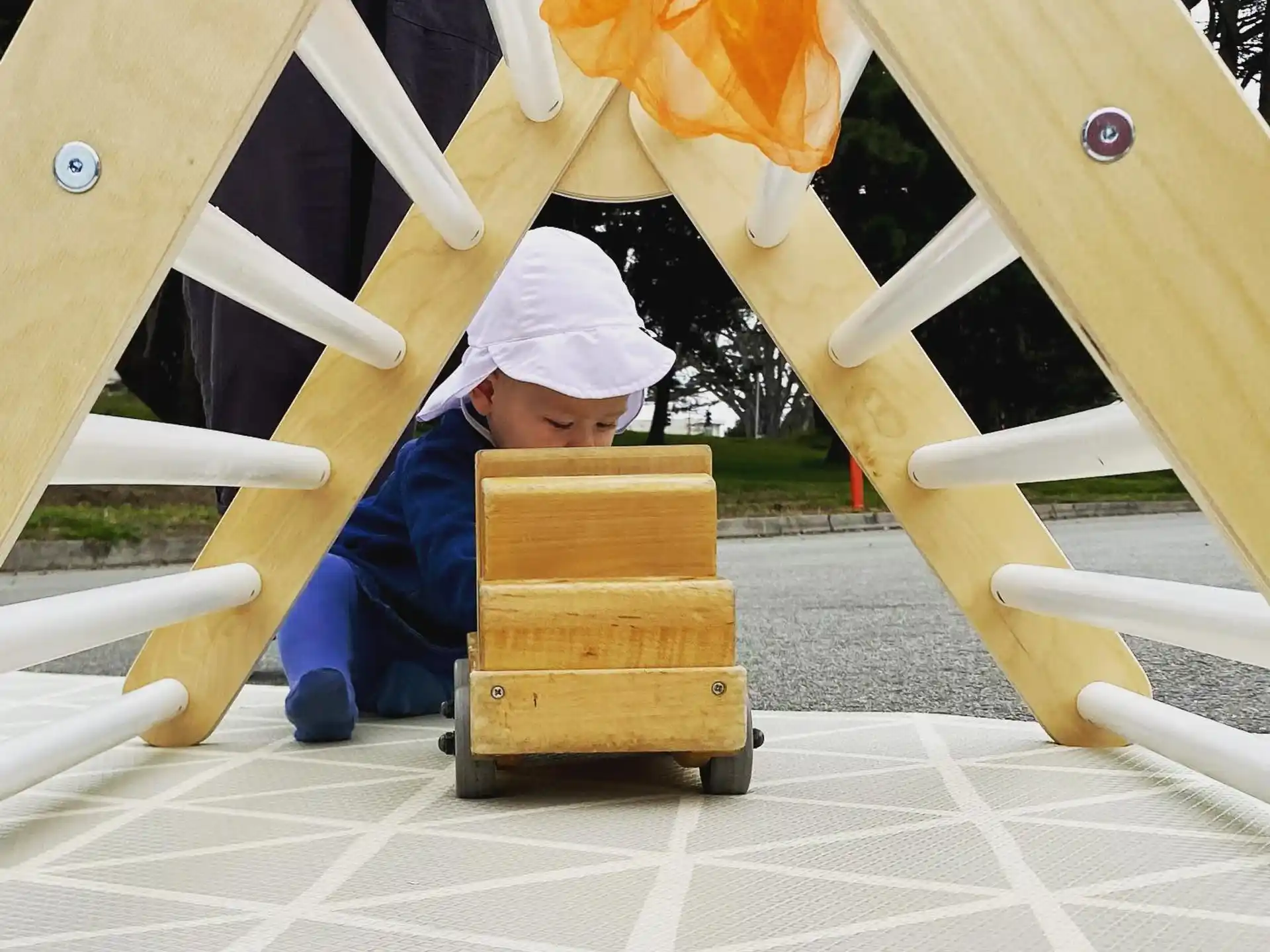 a child in a white hat and blue overalls sitting on a wooden structure