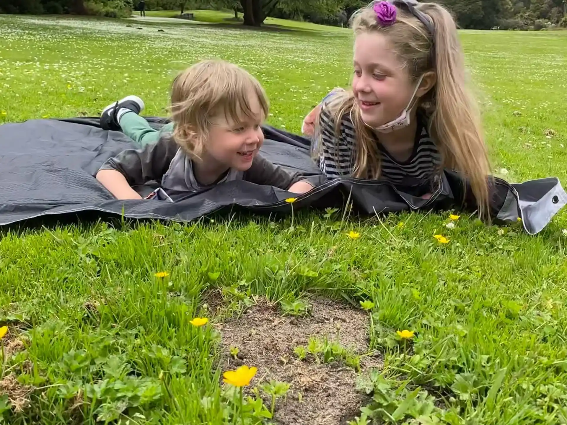 a couple of girls lying in a grassy field with flowers and trees