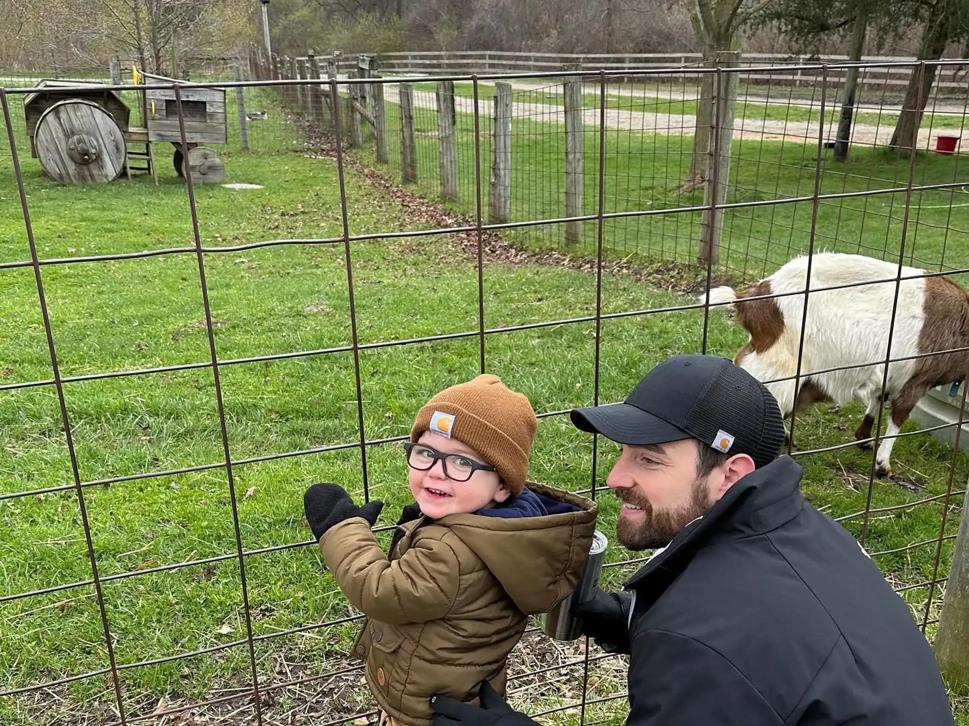 a man and a child by a fence with a sheep in the background