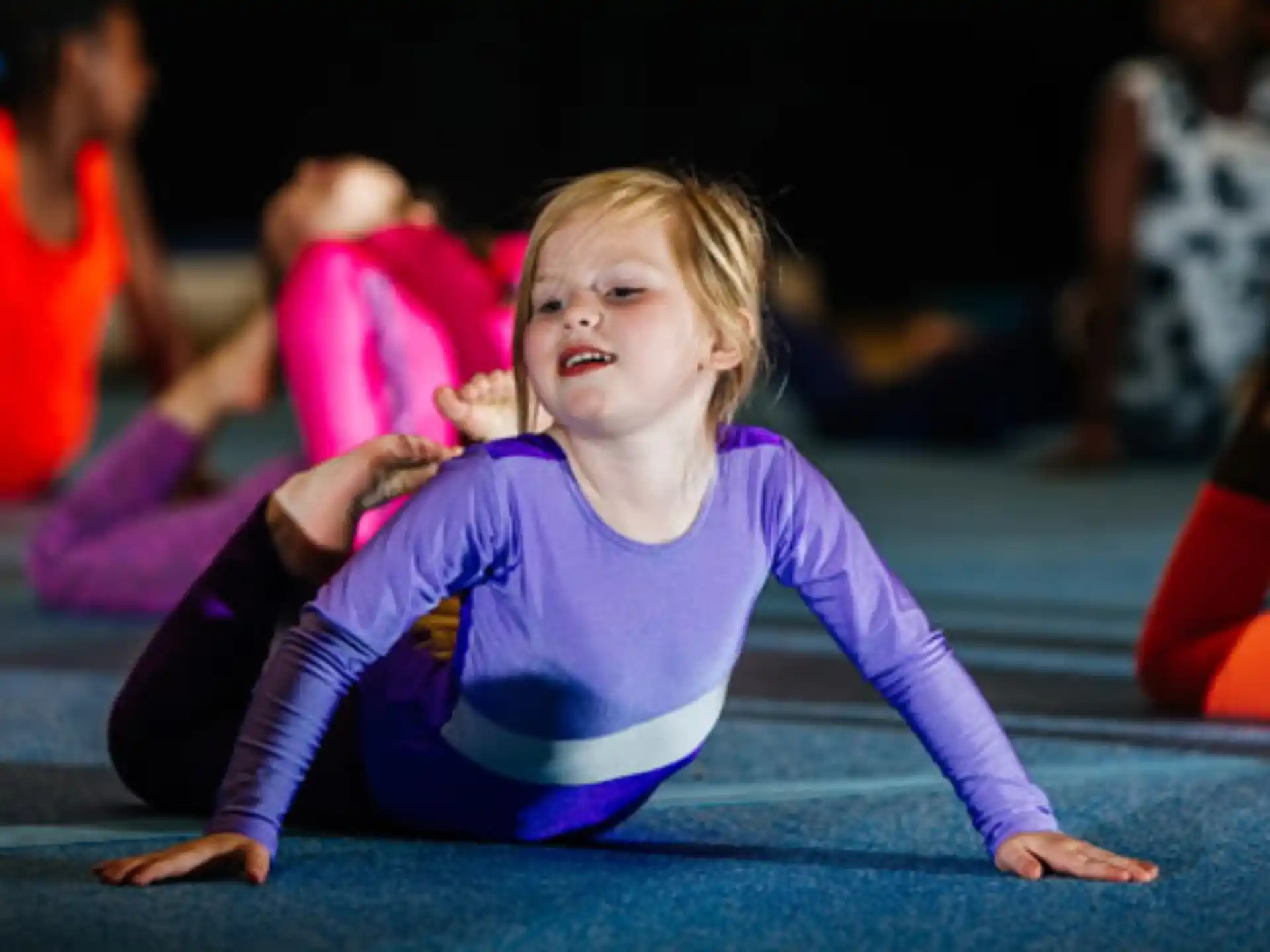 a girl in a purple leotard on a mat
