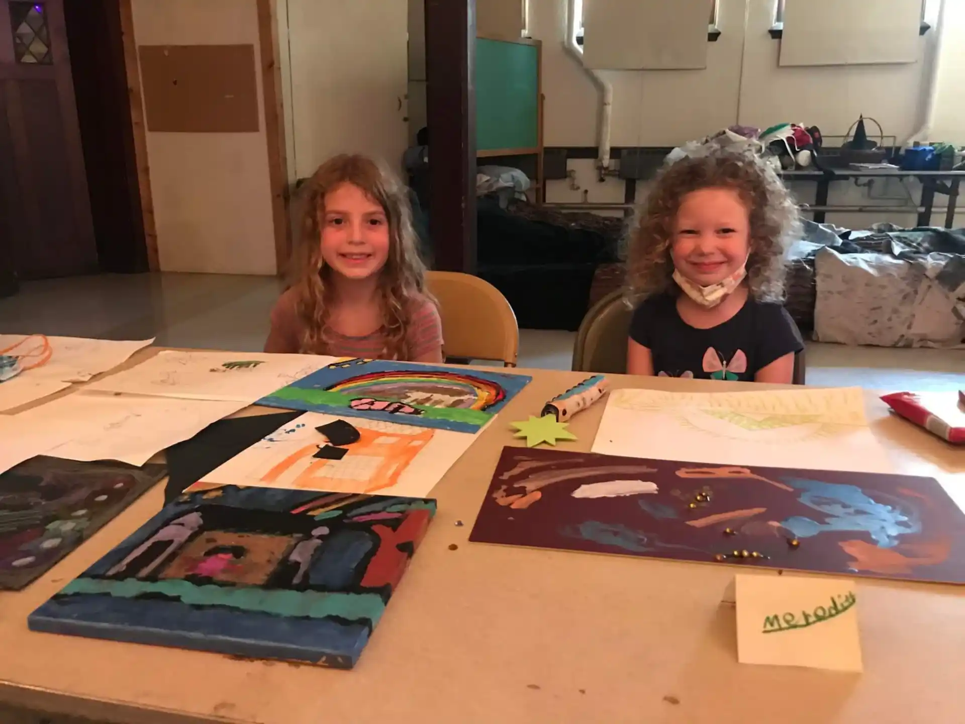 a couple of girls sitting at a table with art on it