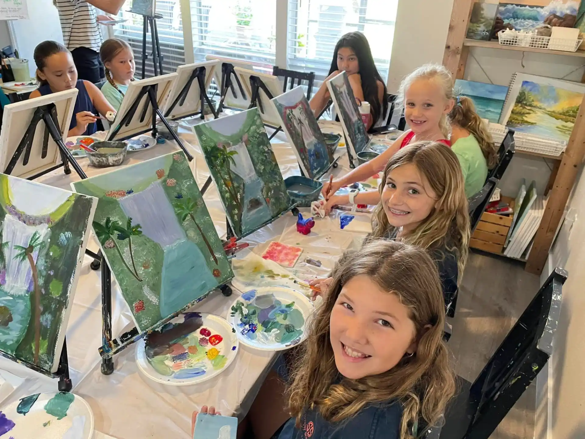 a group of children sitting at a table with art and pictures