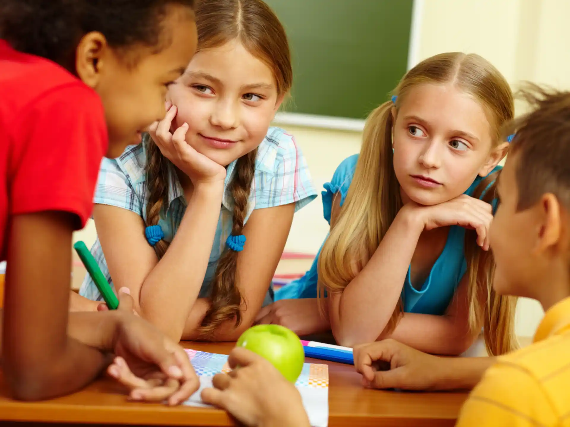 a group of children sitting at a table looking at a green apple