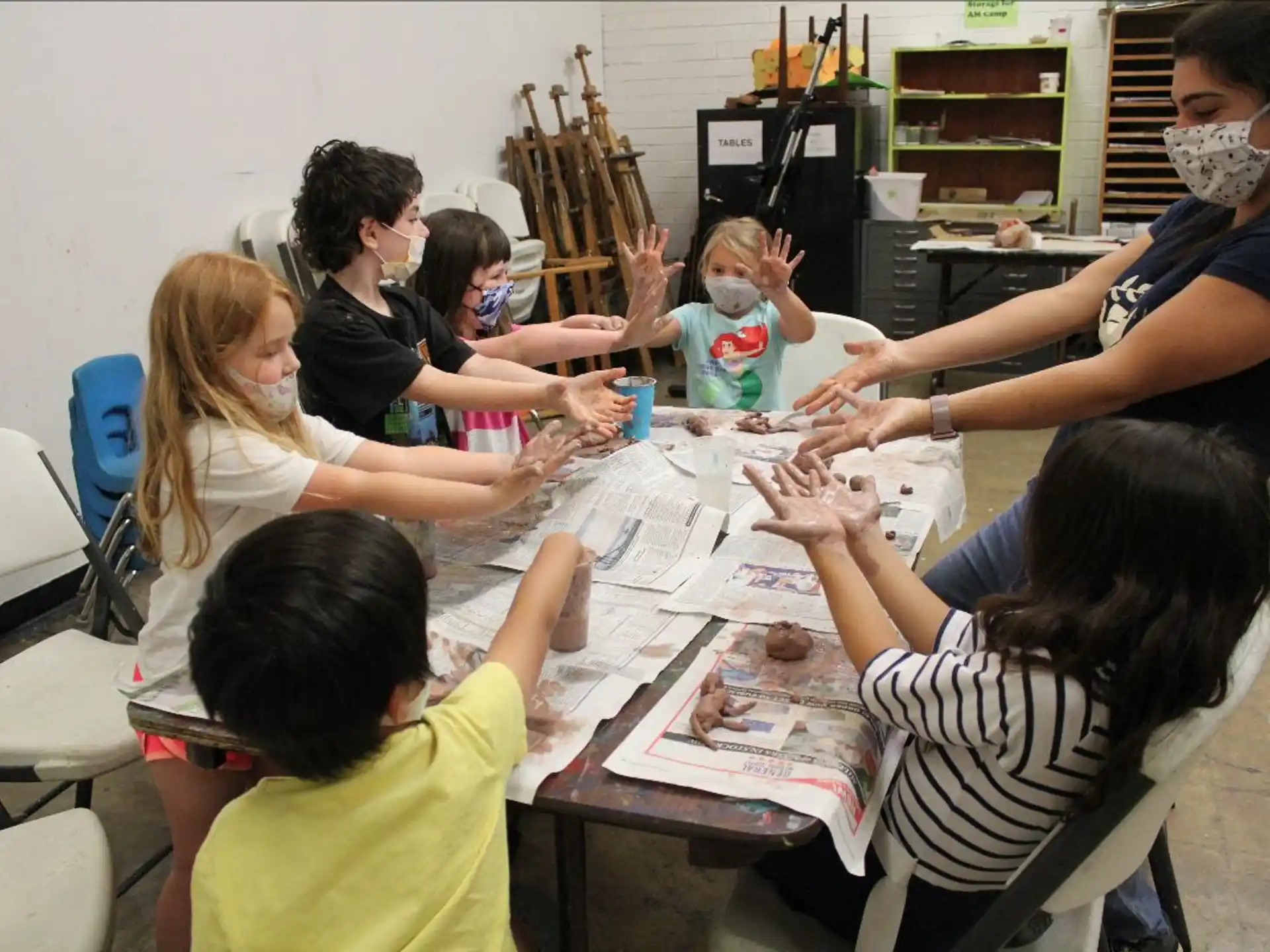 a group of people sitting around a table with a woman wearing a mask