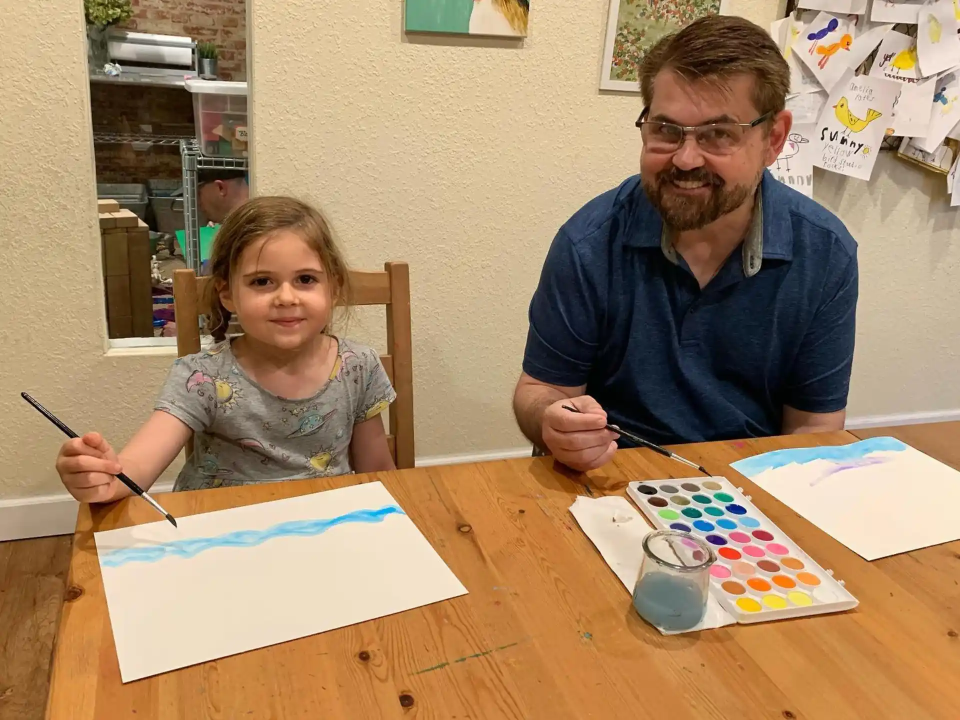 a man and a girl sitting at a table with art