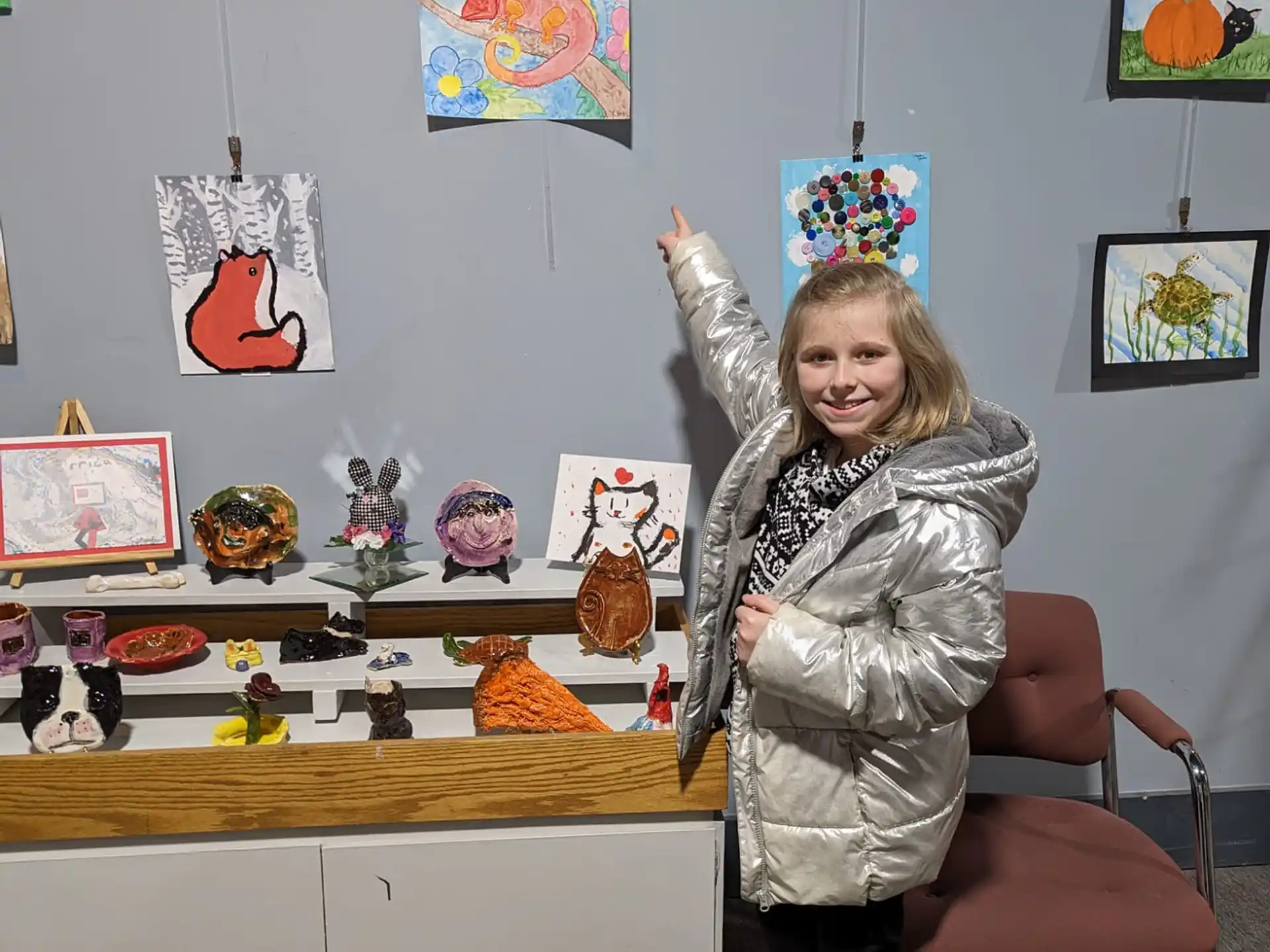 a girl standing in front of a desk with a chair and a shelf with toys on it