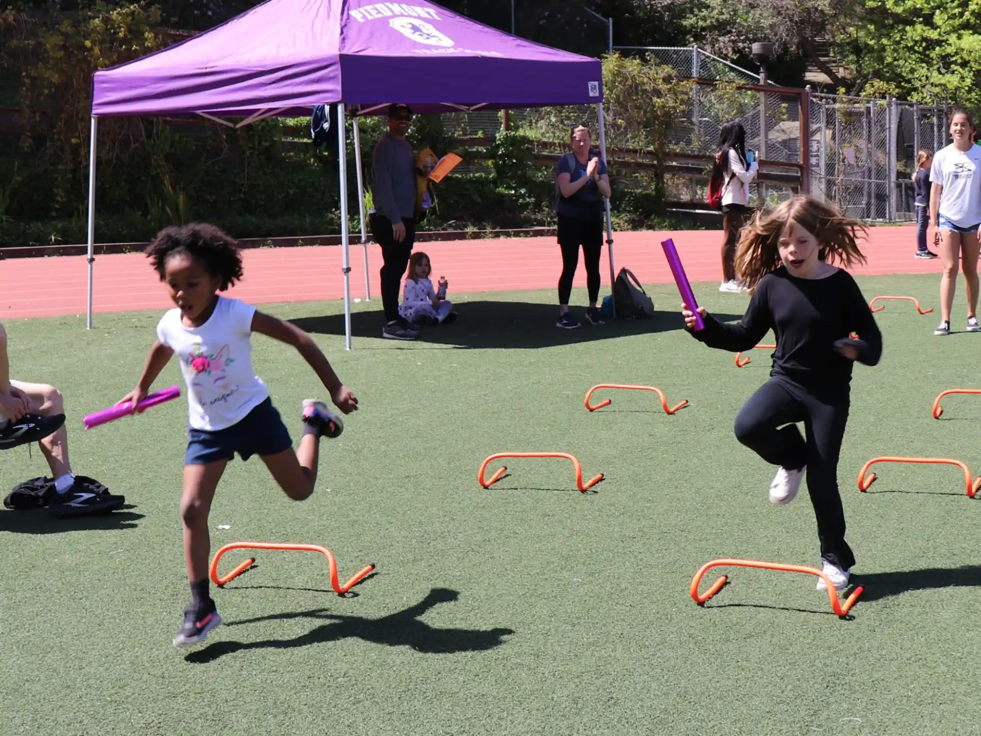 a couple of girls running on a field with a tent and people in the background