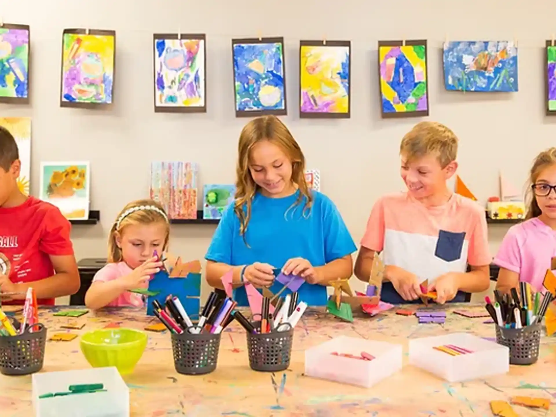 a group of children sitting at a table with art on the wall