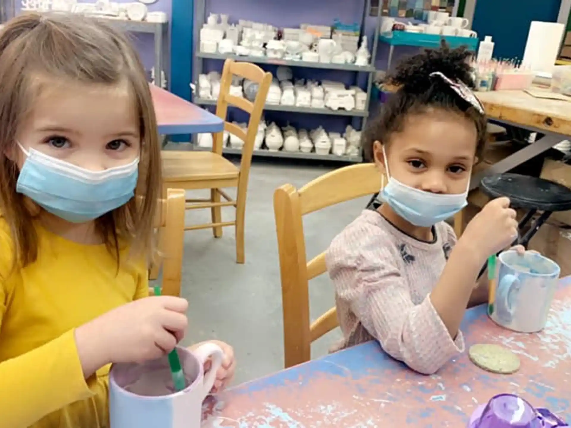 a couple of young girls wearing face masks and sitting at a table