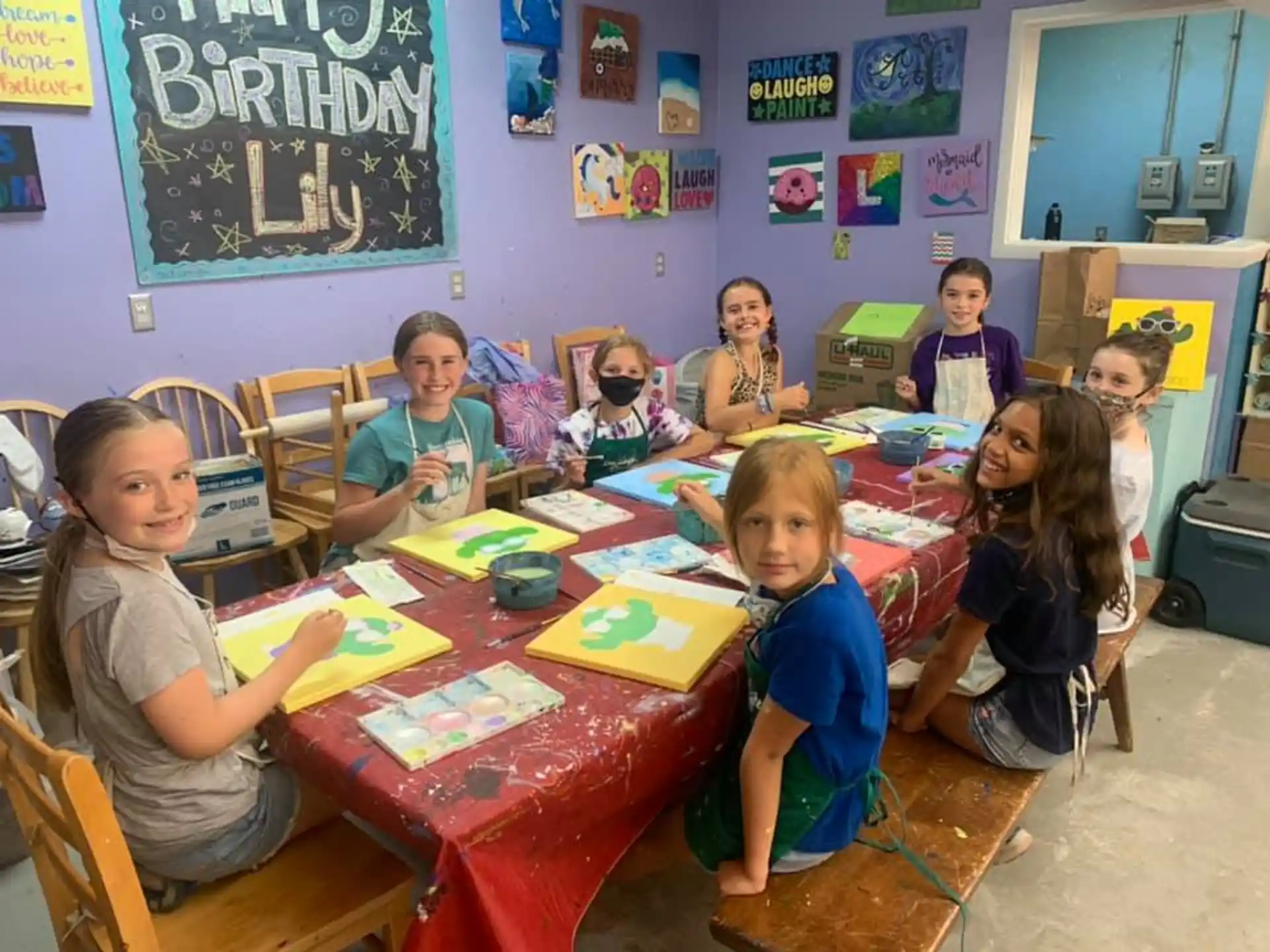 a group of children sitting at a table with a red tablecloth