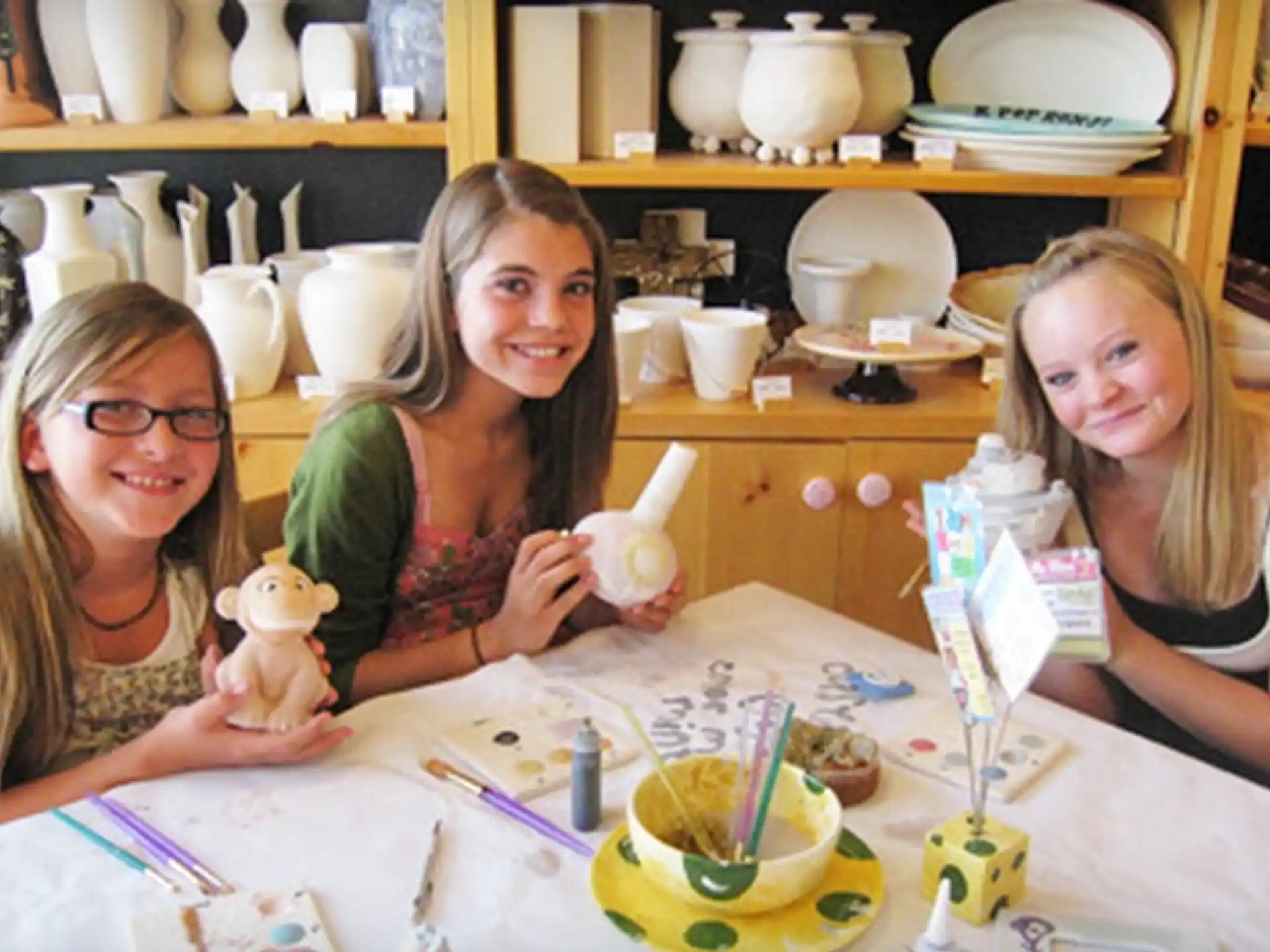 a group of girls sitting at a table with a doll and a teapot