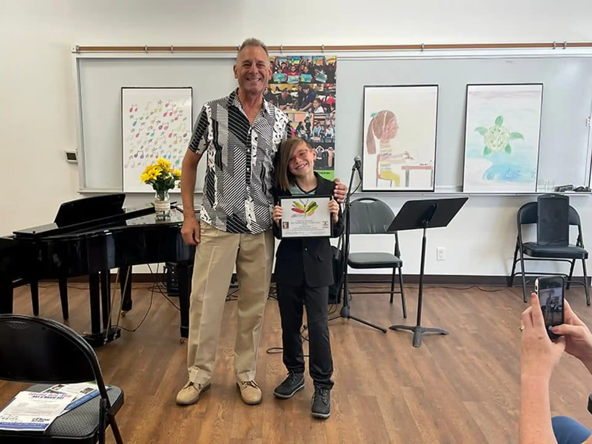 a man and a woman holding a certificate in a room with chairs and a piano