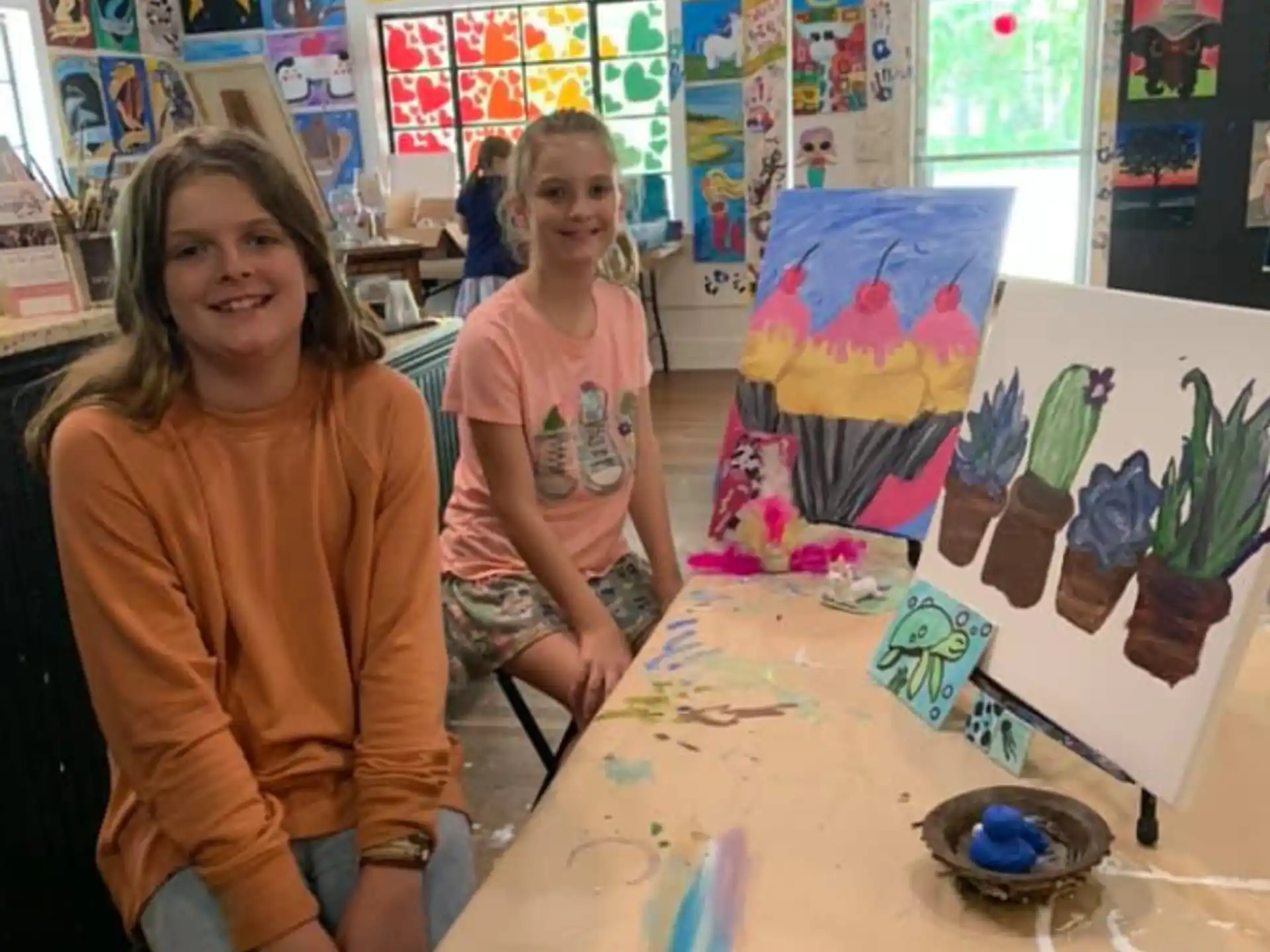 a couple of girls sitting at a table with art on it