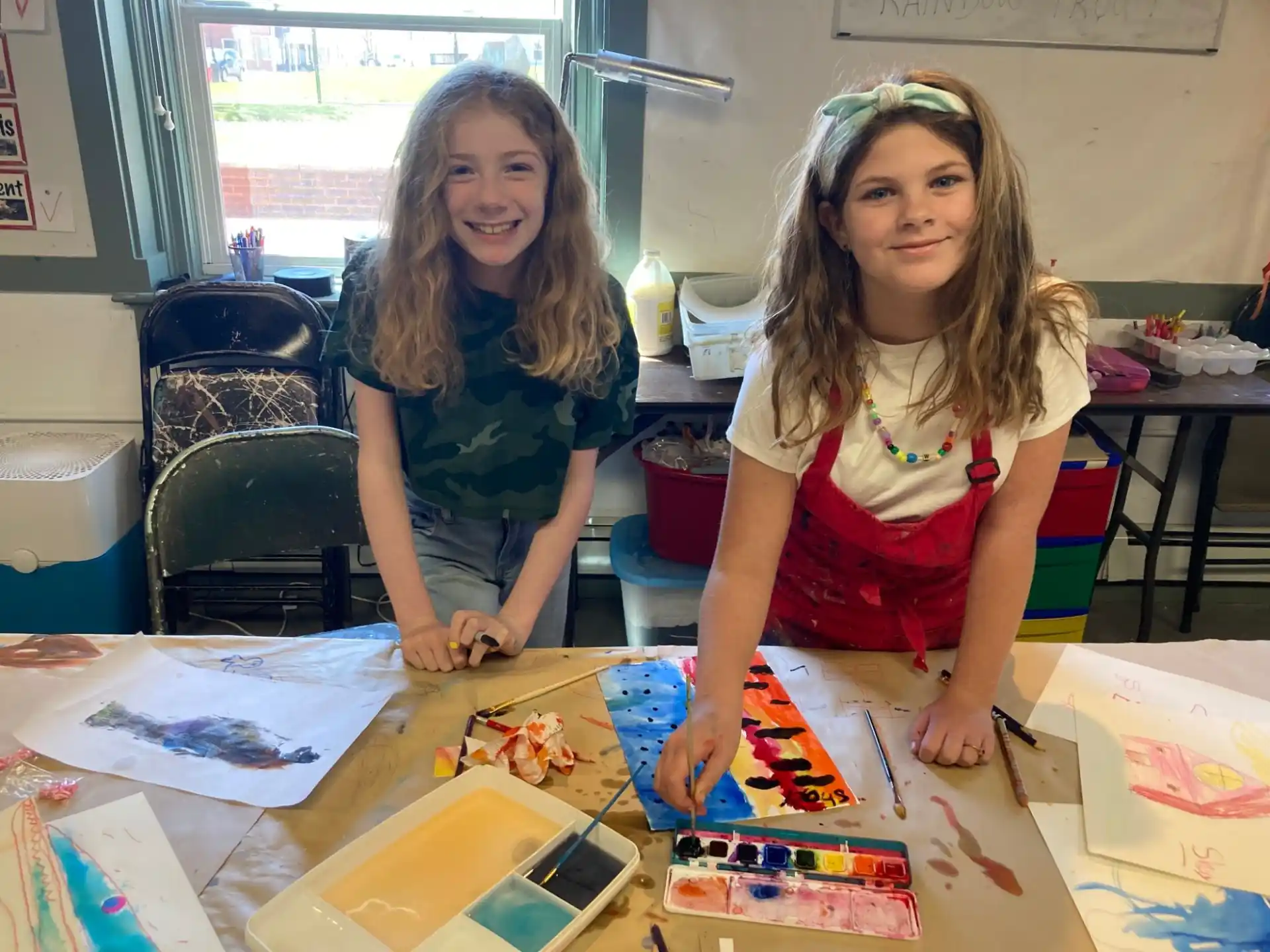 a couple of girls sitting at a table with art
