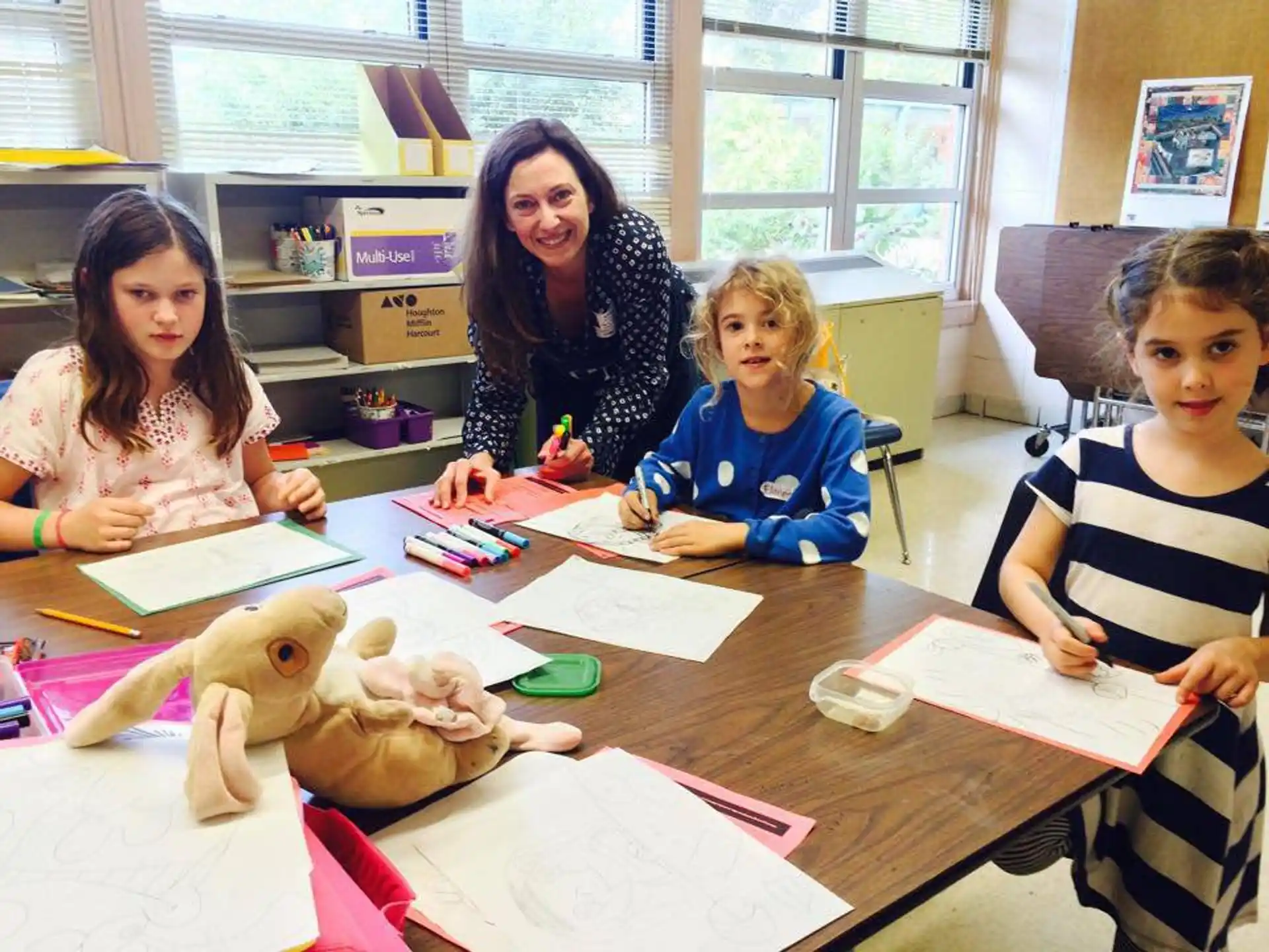 a group of children sitting at a table with a stuffed animal