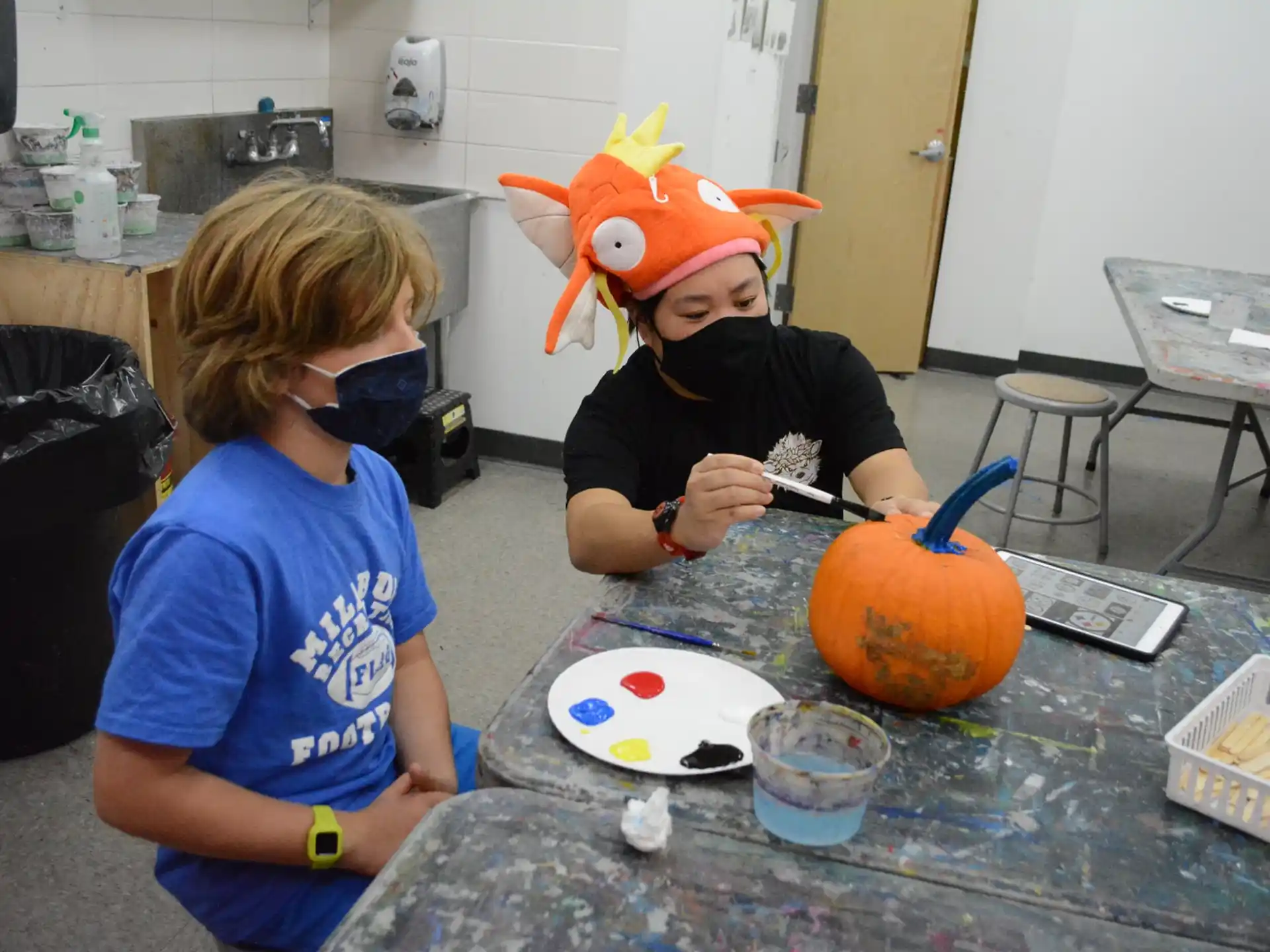 a couple of kids sitting at a table with a pumpkin and a knife