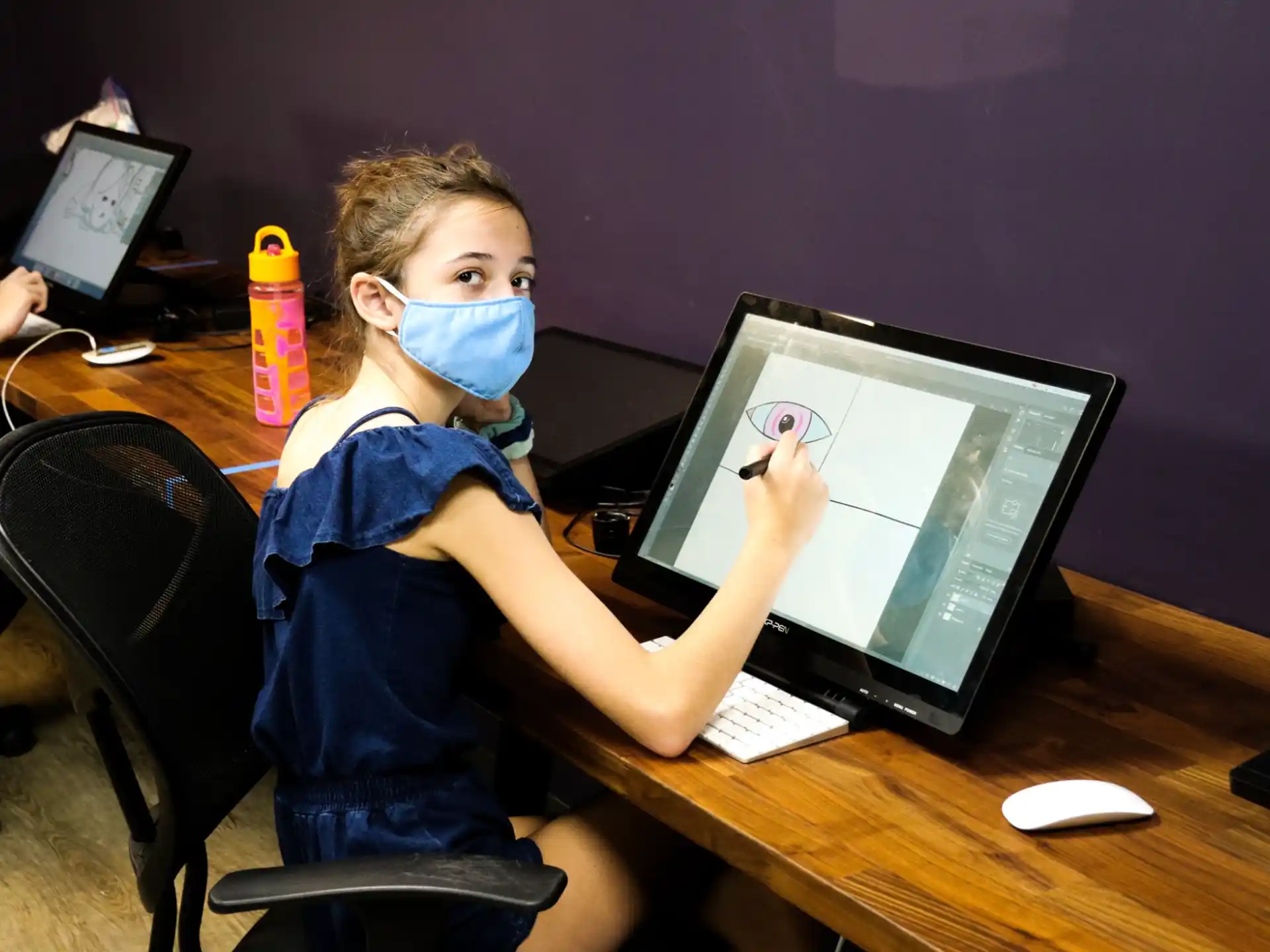 a young boy wearing a mask and sitting at a desk with a computer