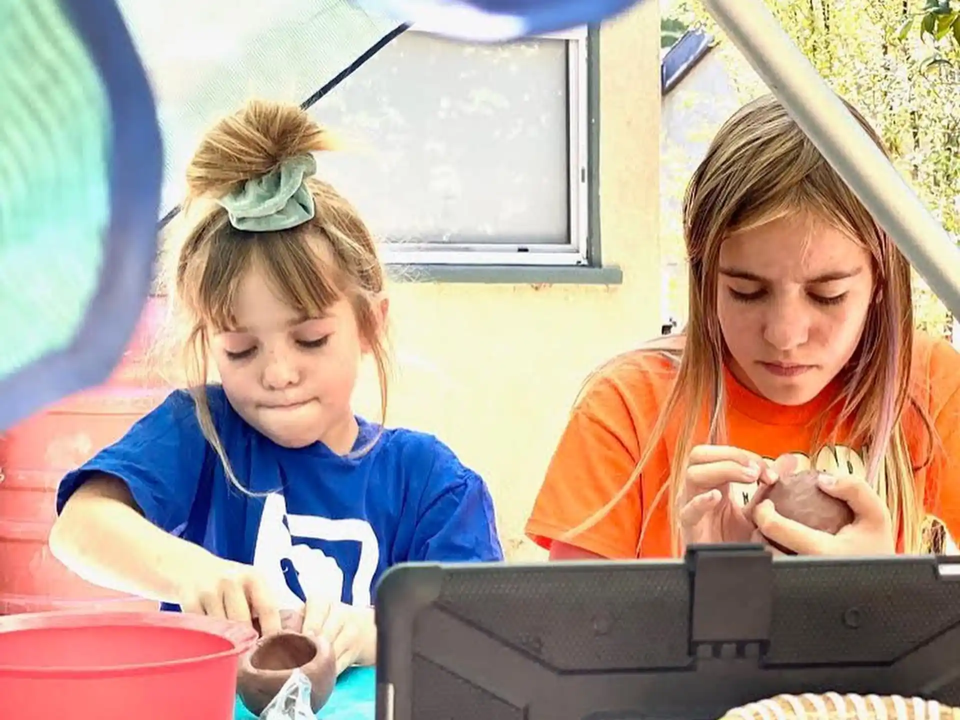 a couple of girls sitting at a table with a laptop and a basket of food
