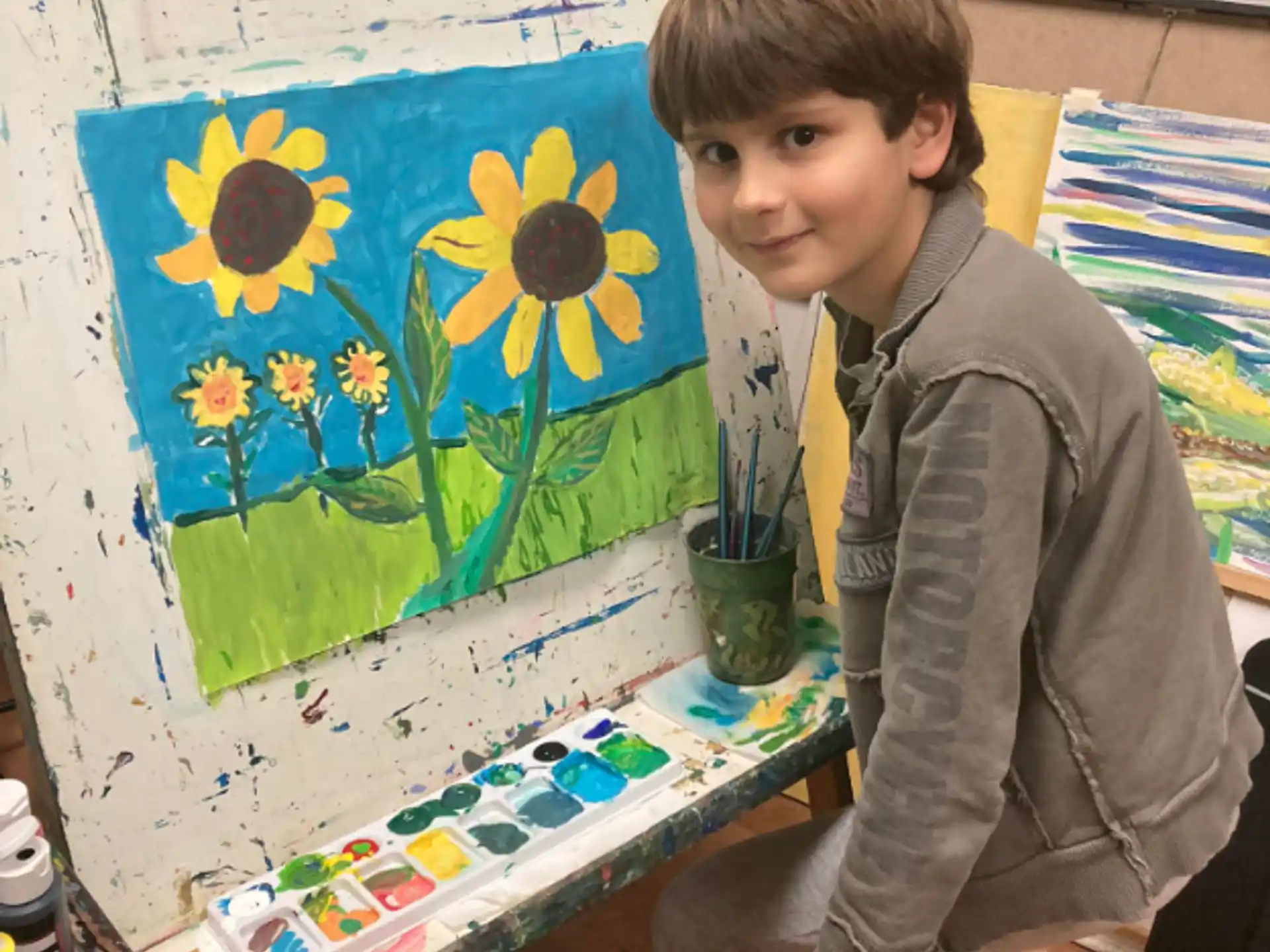 a boy sitting next to a painting