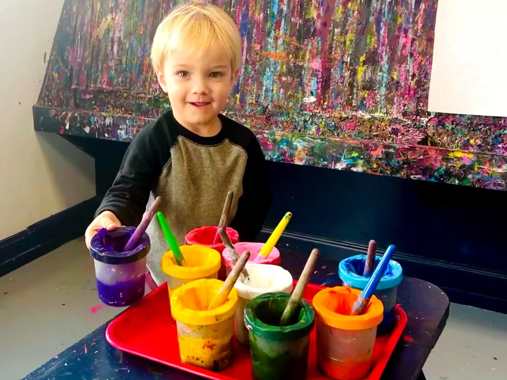 a child sitting at a table with colorful cups and a blue tablecloth