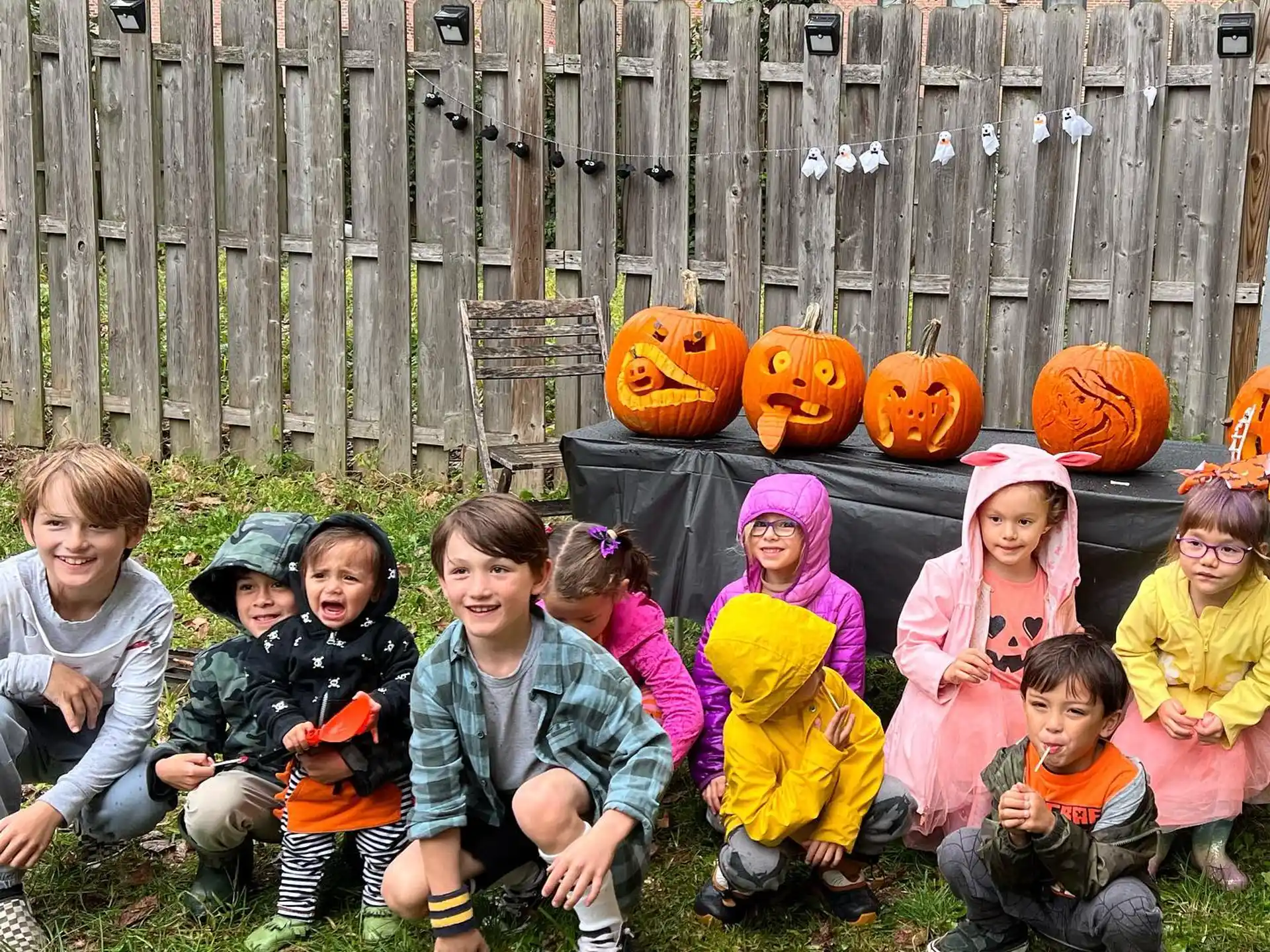 a group of children sitting on the grass with pumpkins in the background