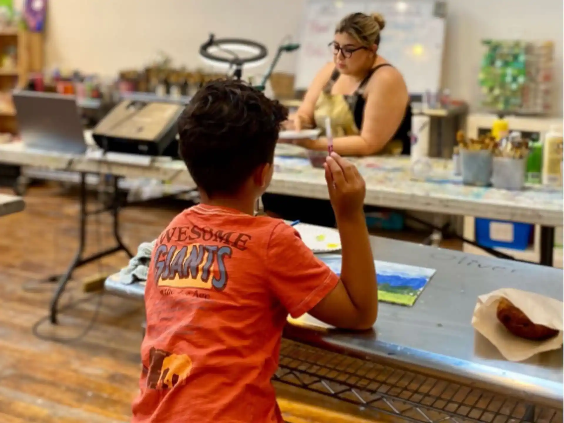 a boy sitting at a table with a person in the background