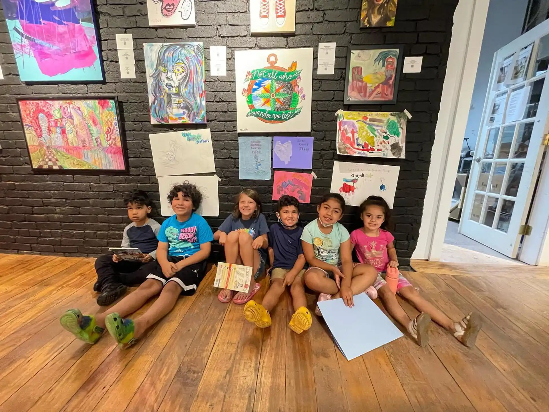a group of children sitting on the floor in front of a wall with art