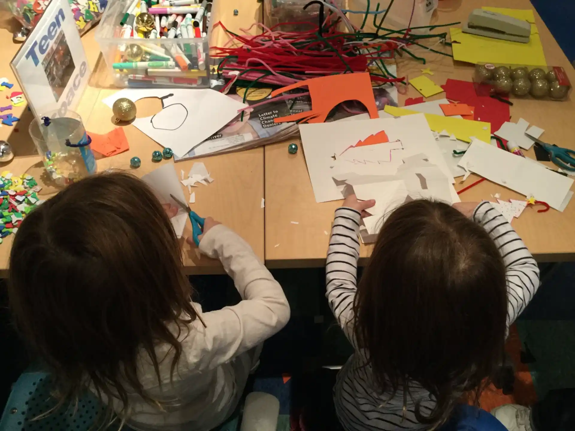 a couple of girls sitting at a table with papers and pencils