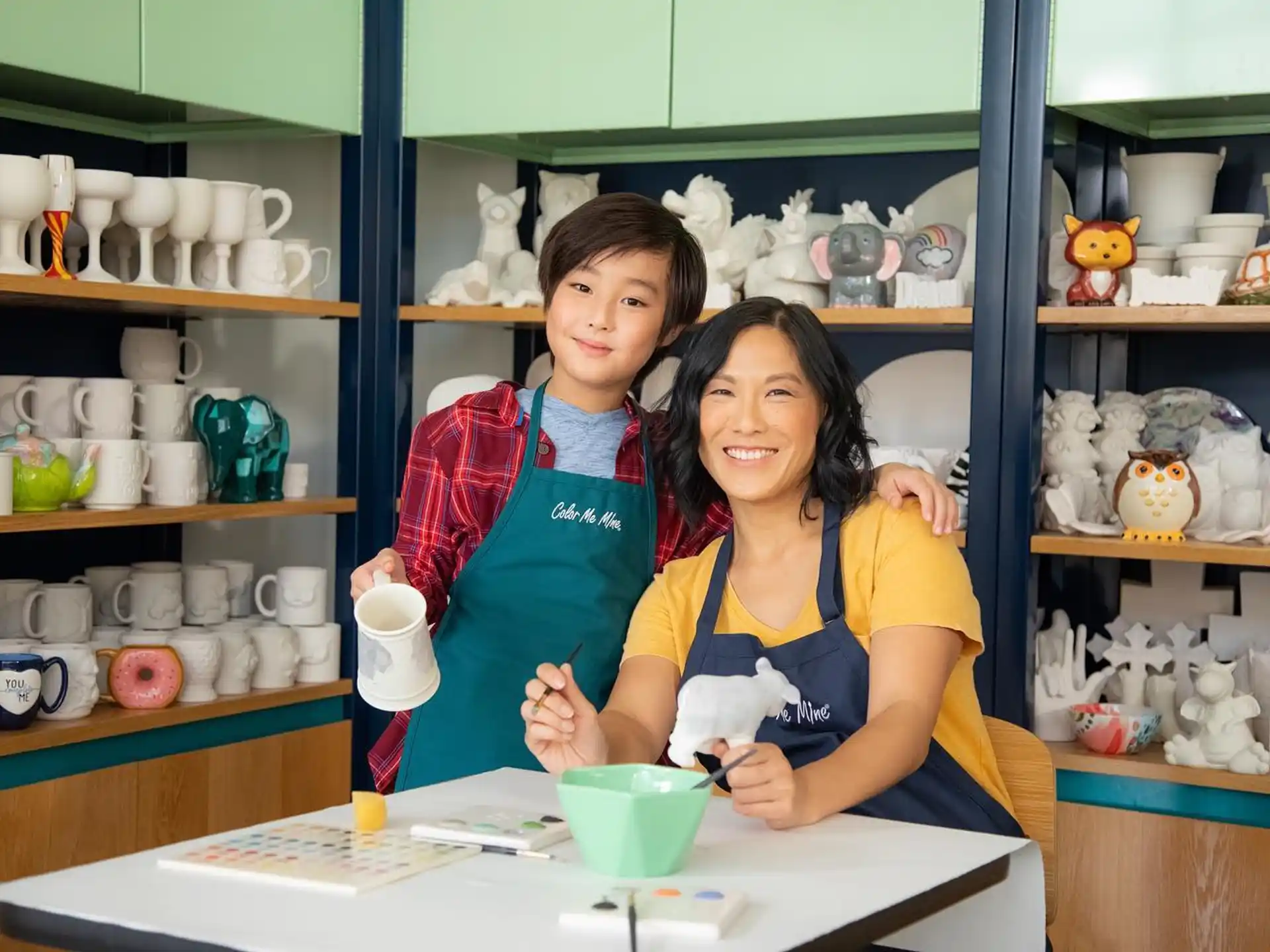 a woman and a boy in a room with shelves and cups