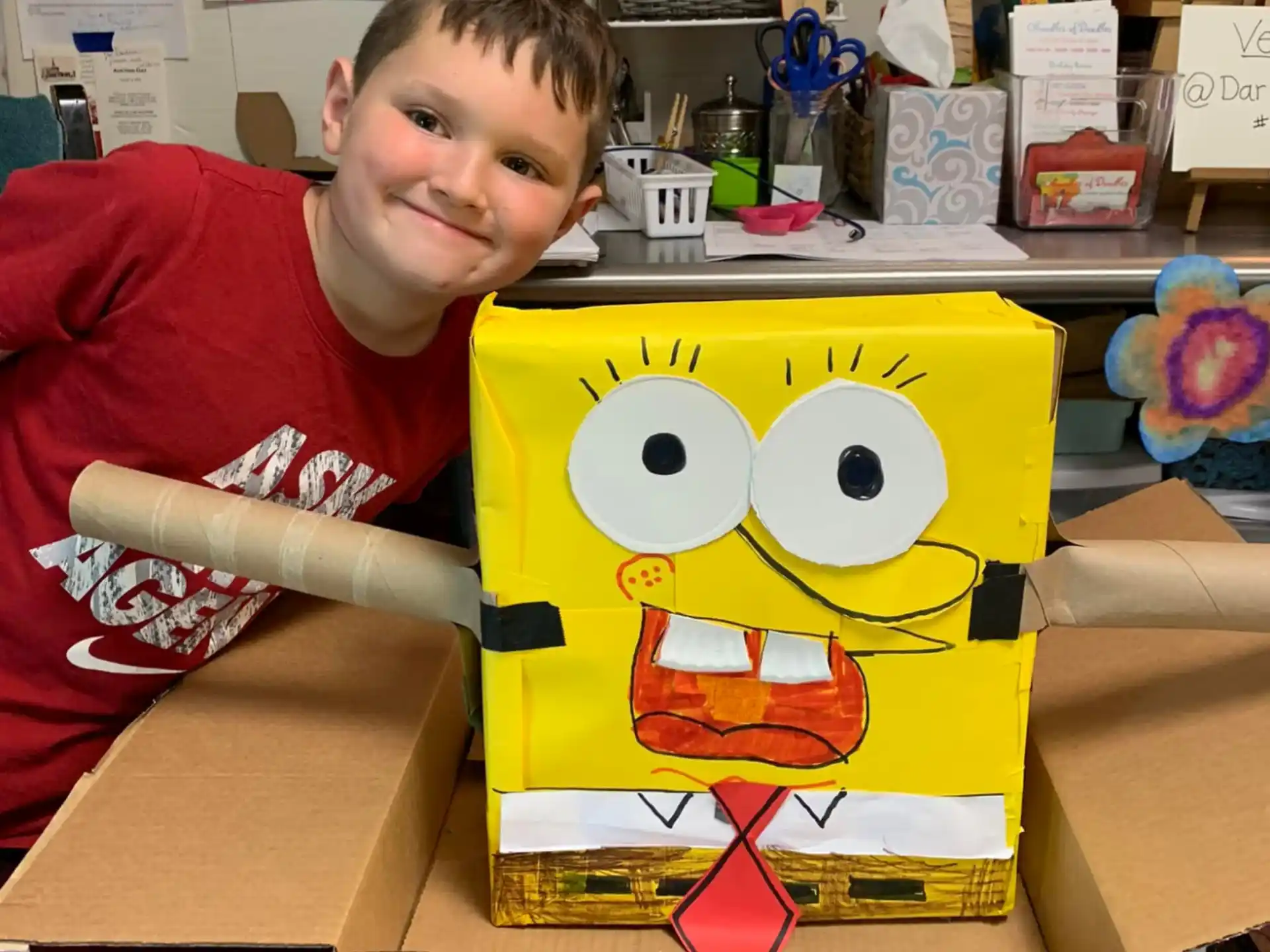 a boy sitting at a table with a yellow and red stuffed animal