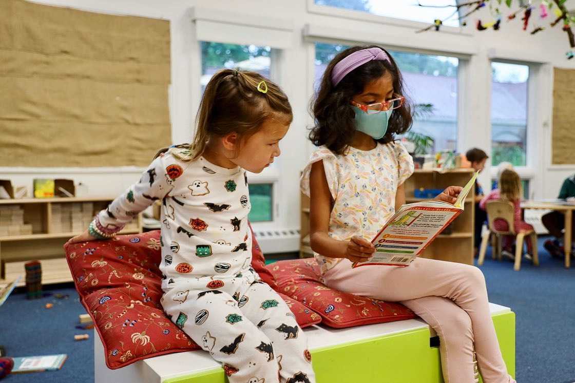 a couple of girls sitting on a bench reading a book
