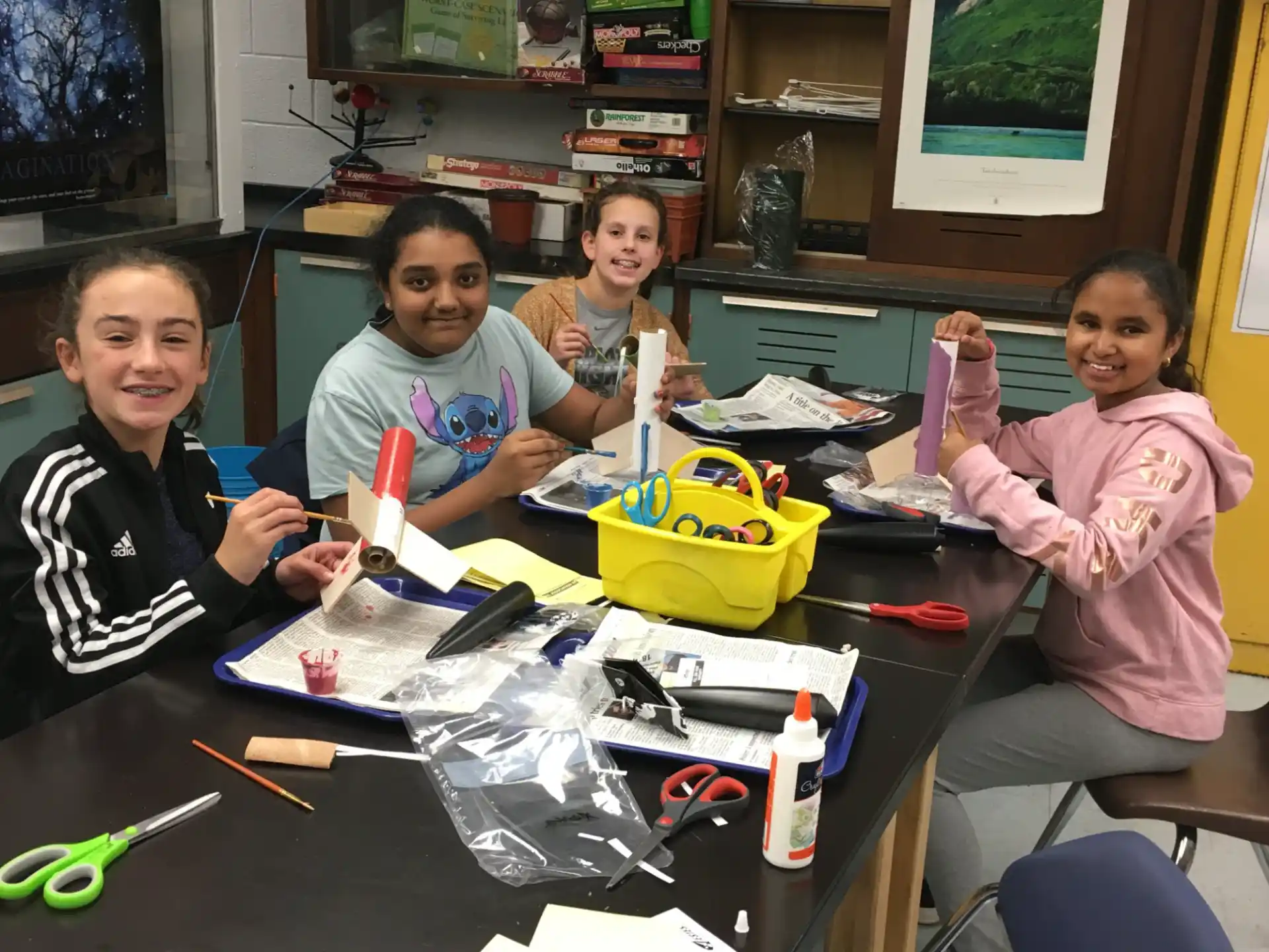 a group of children sitting at a table with tools and a bookcase