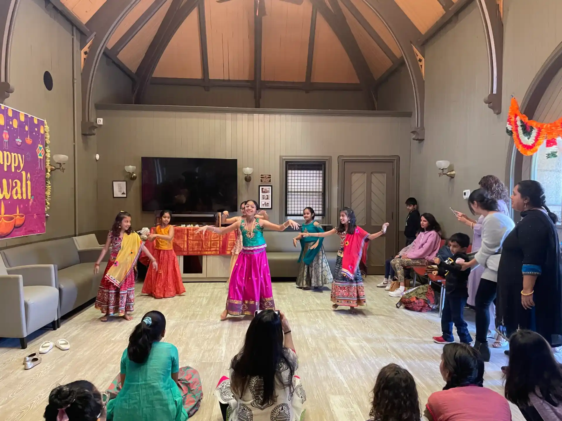 a group of children dancing in a room with a television and people watching