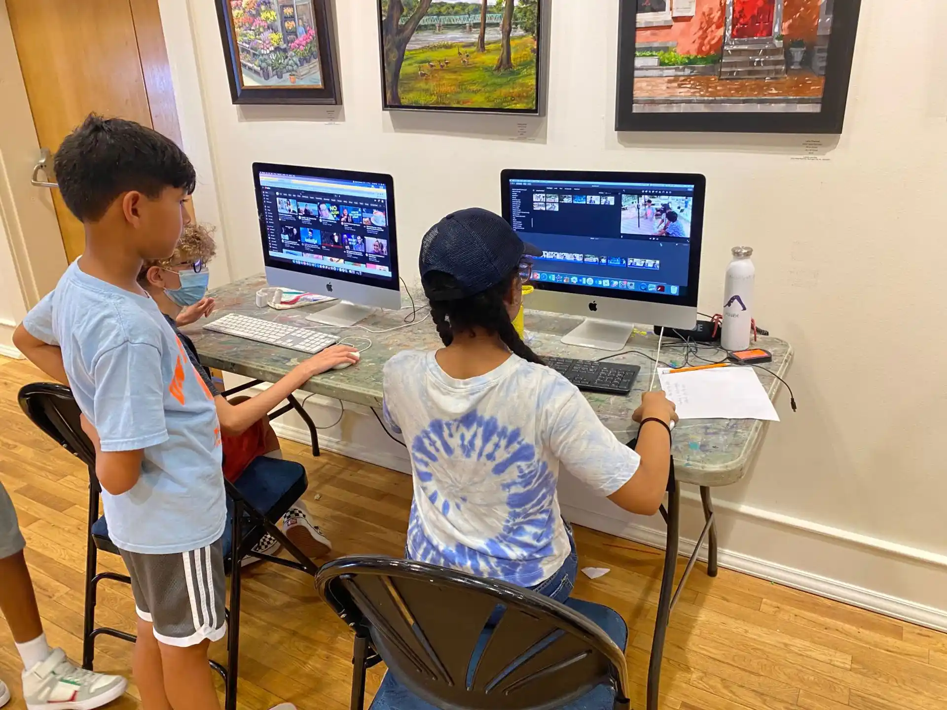 a couple of kids sitting at a desk with computers