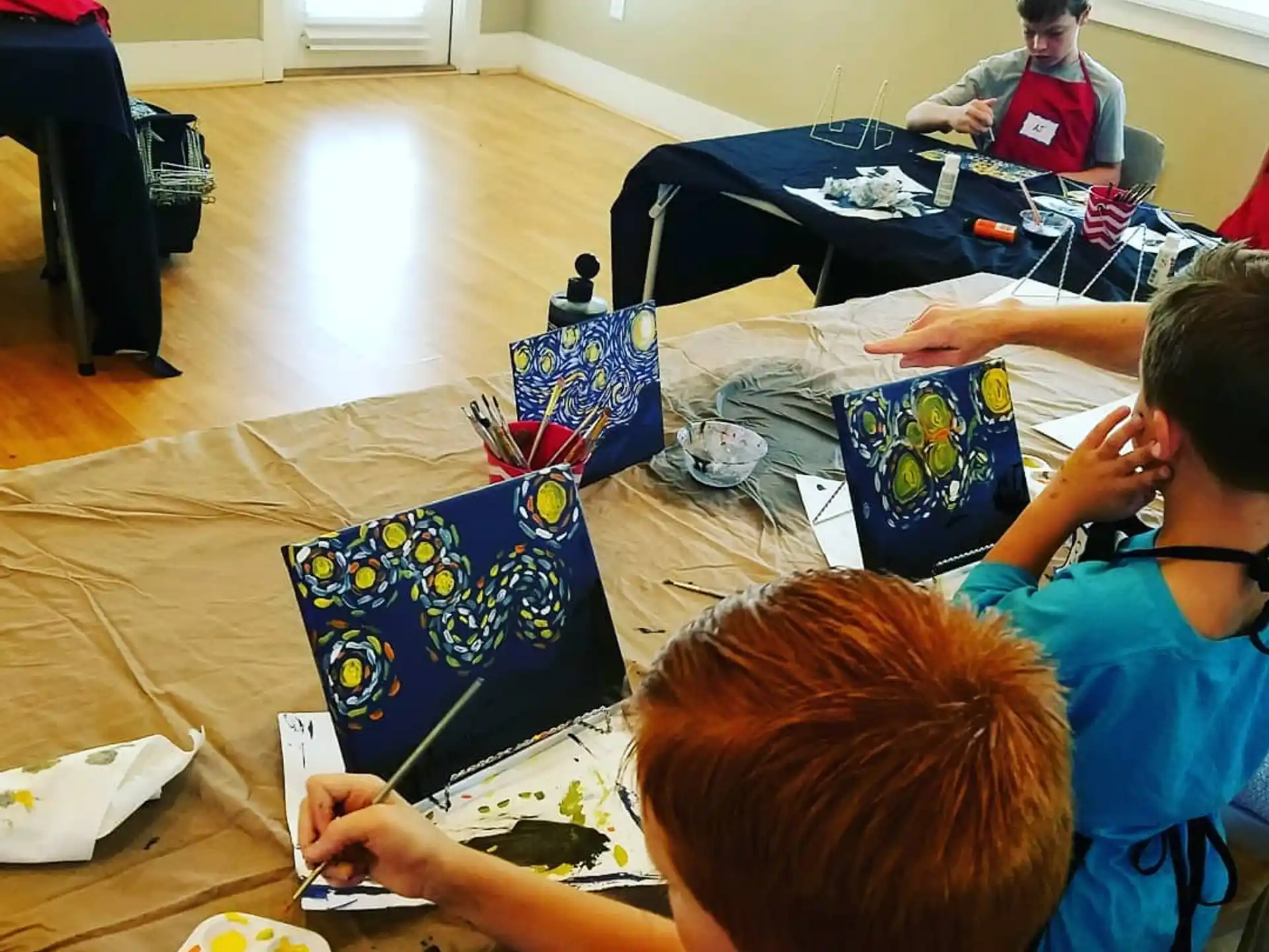 a group of kids sitting at a table with a laptop and a person standing behind them