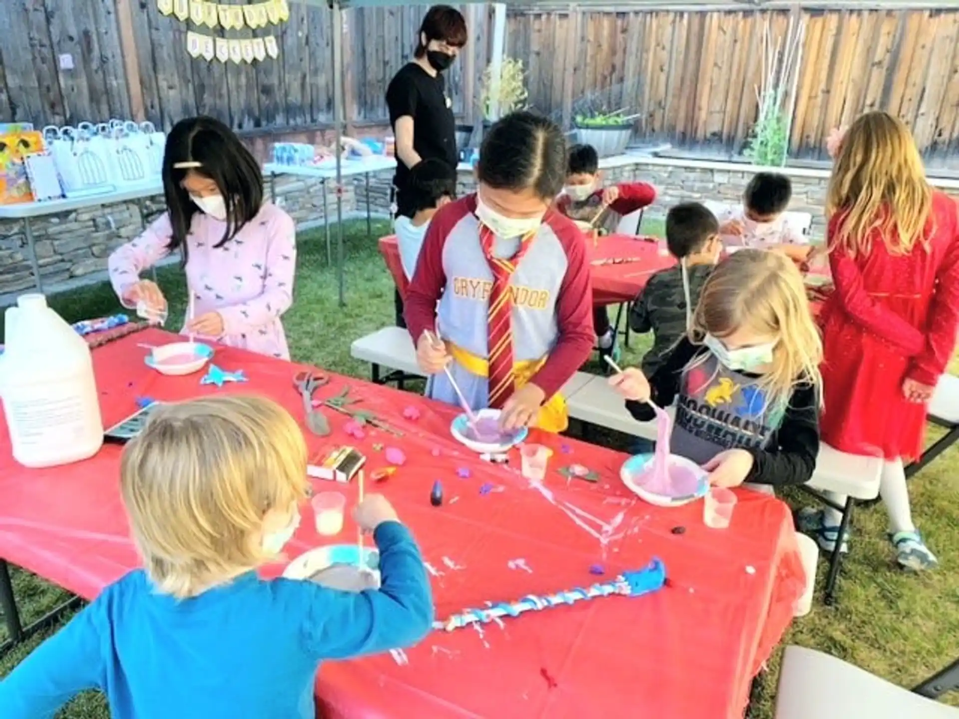 a group of children sitting around a table with a red tablecloth
